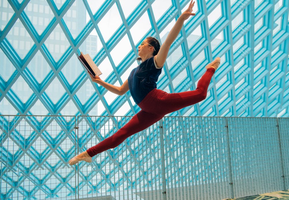 A female dancer leaps through the Seattle public library while reading