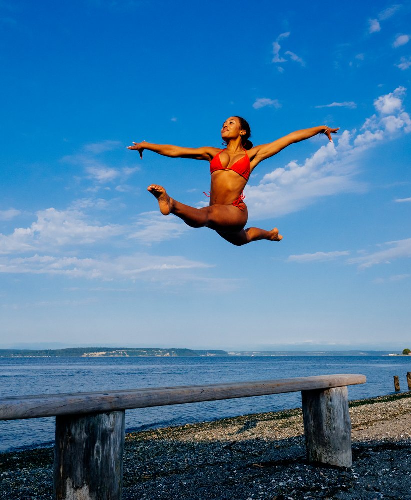 Woman in red swimwear performing a high leap on a beach balance beam
