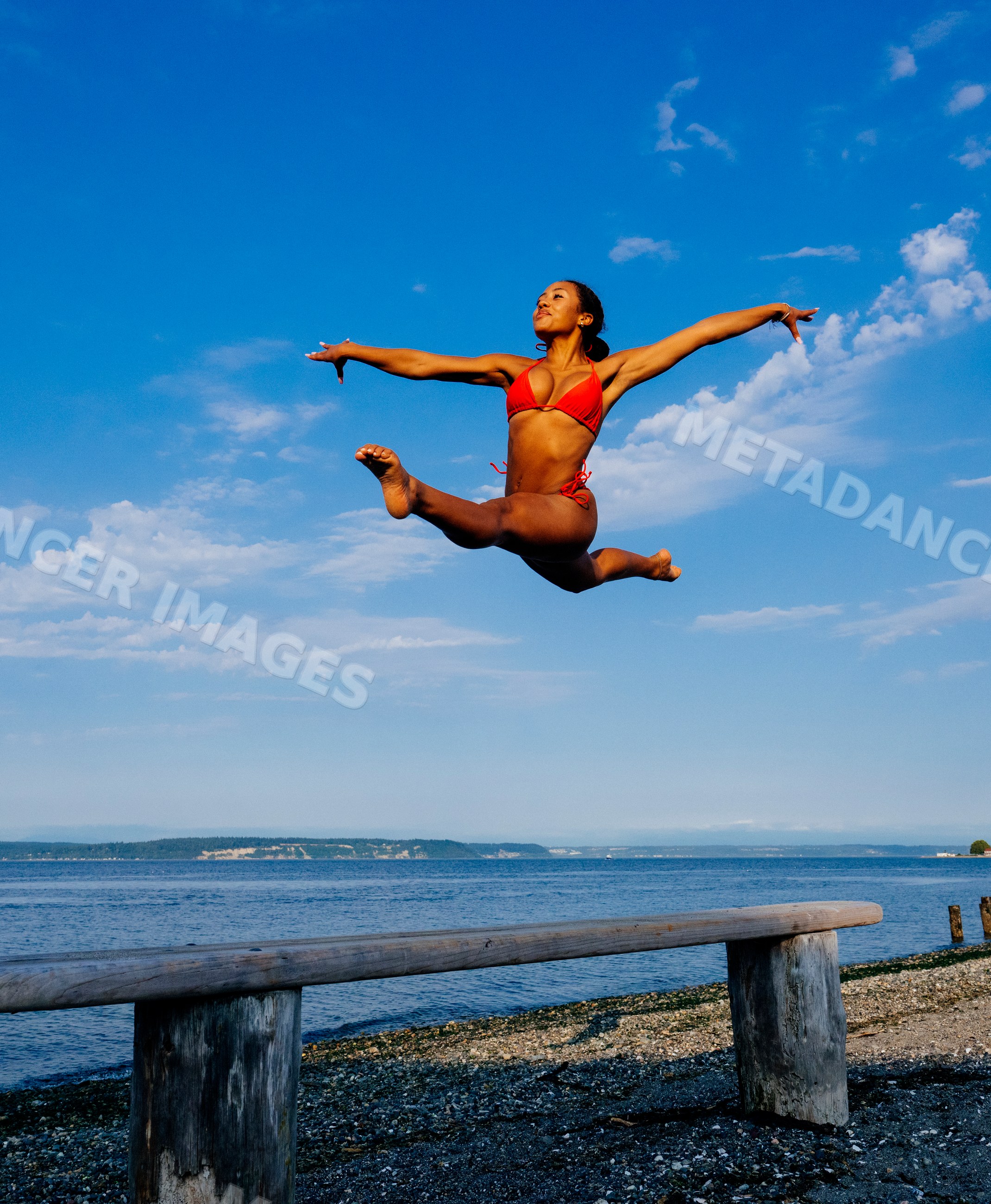 Woman in red swimwear performing a high leap on a beach balance beam