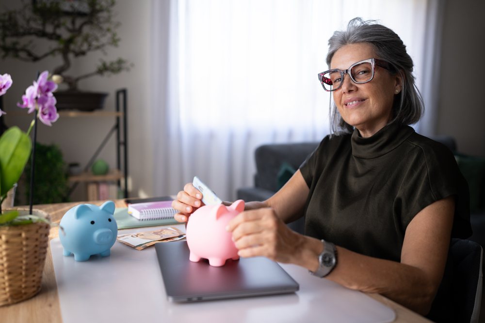 Mature white woman saving money with piggy banks at home