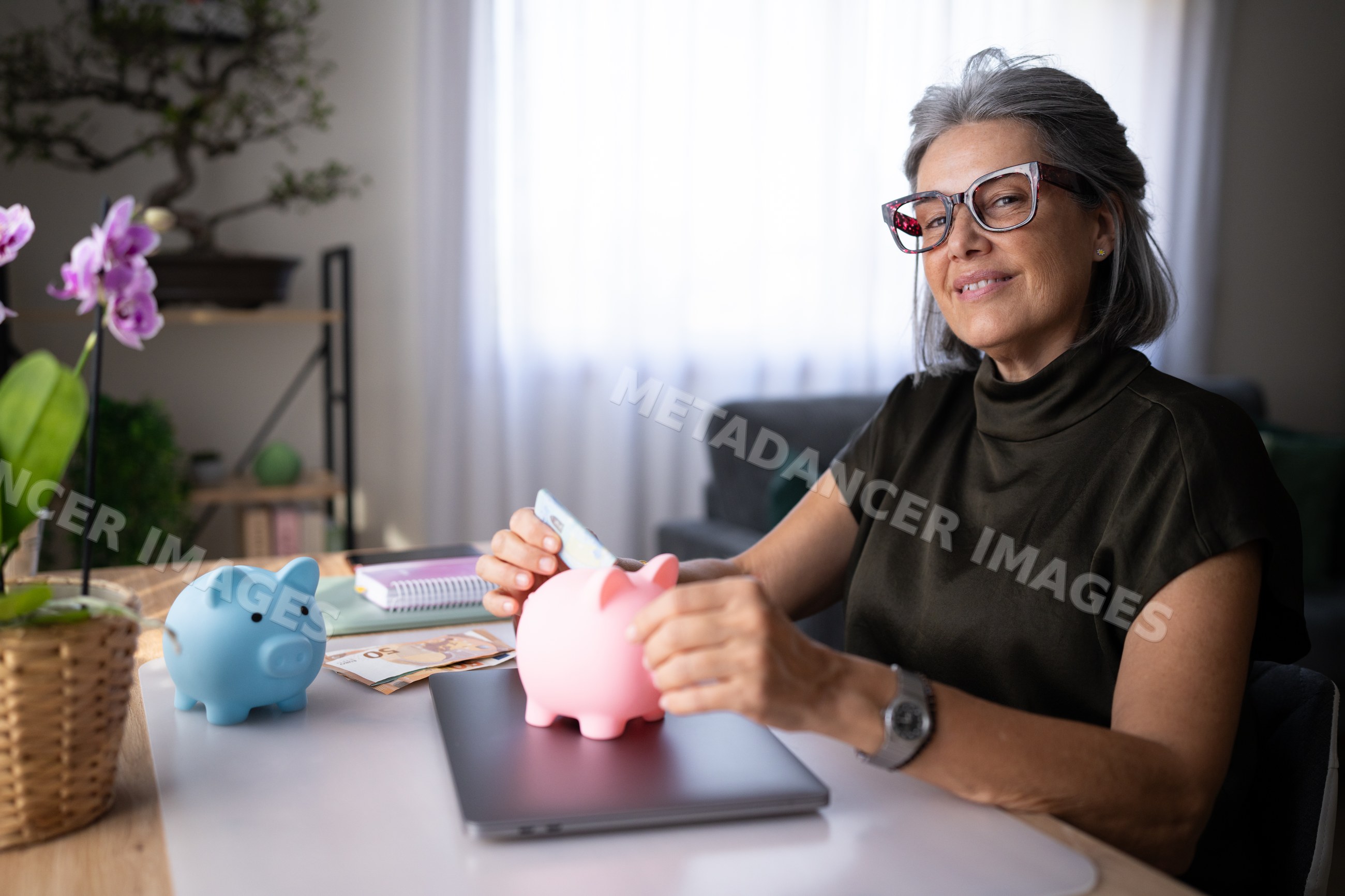 Mature white woman saving money with piggy banks at home