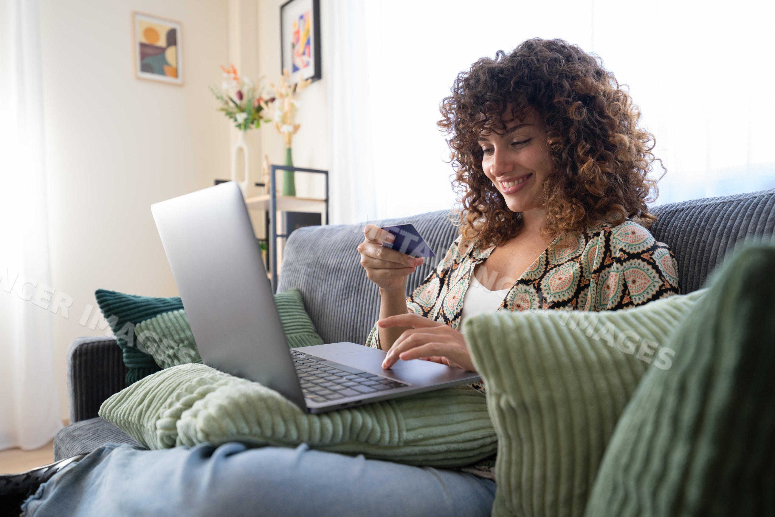 White woman with curly hair using laptop and holding credit card