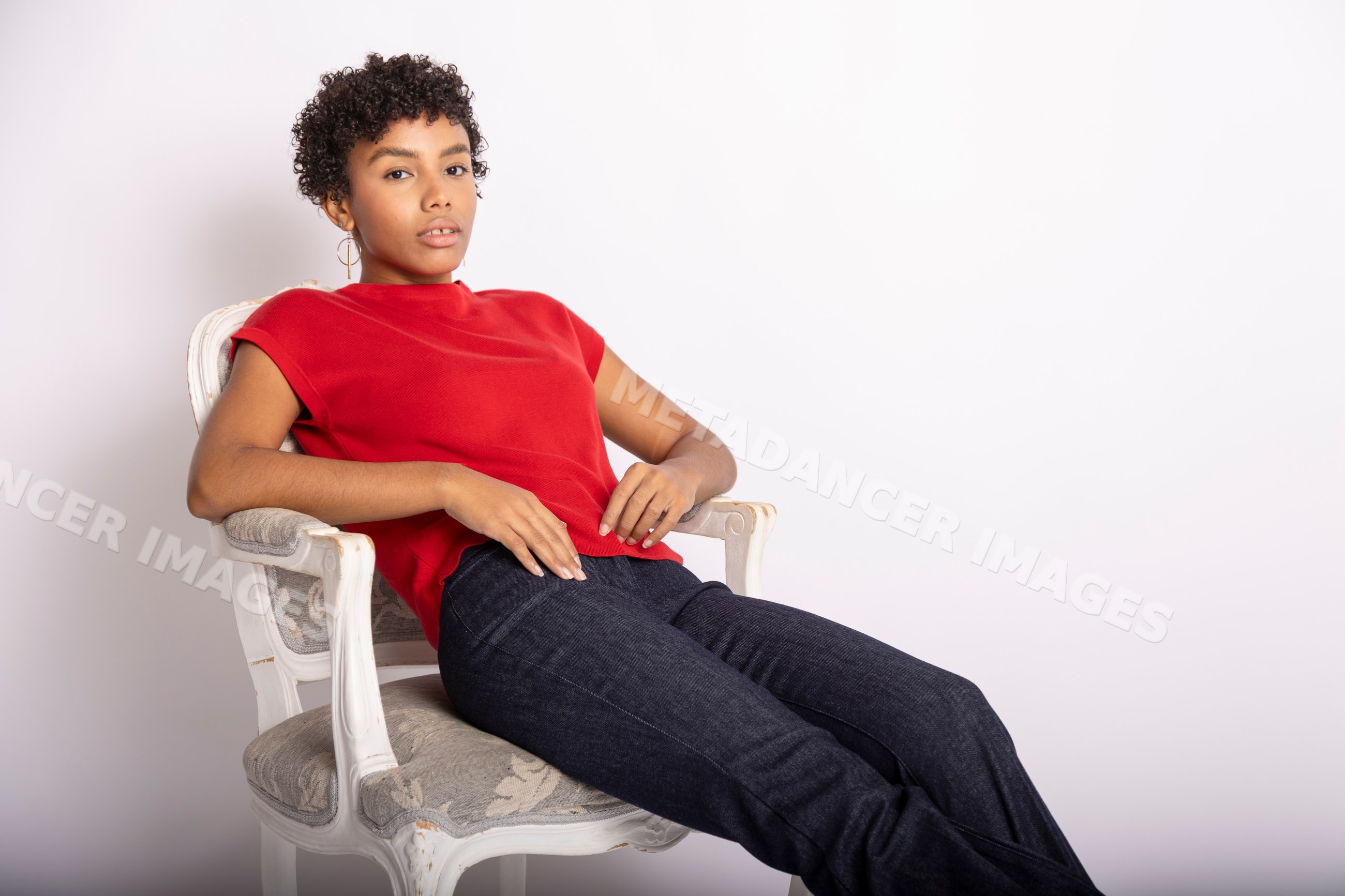 Hispanic woman sitting in red shirt and jeans on upholstered chair