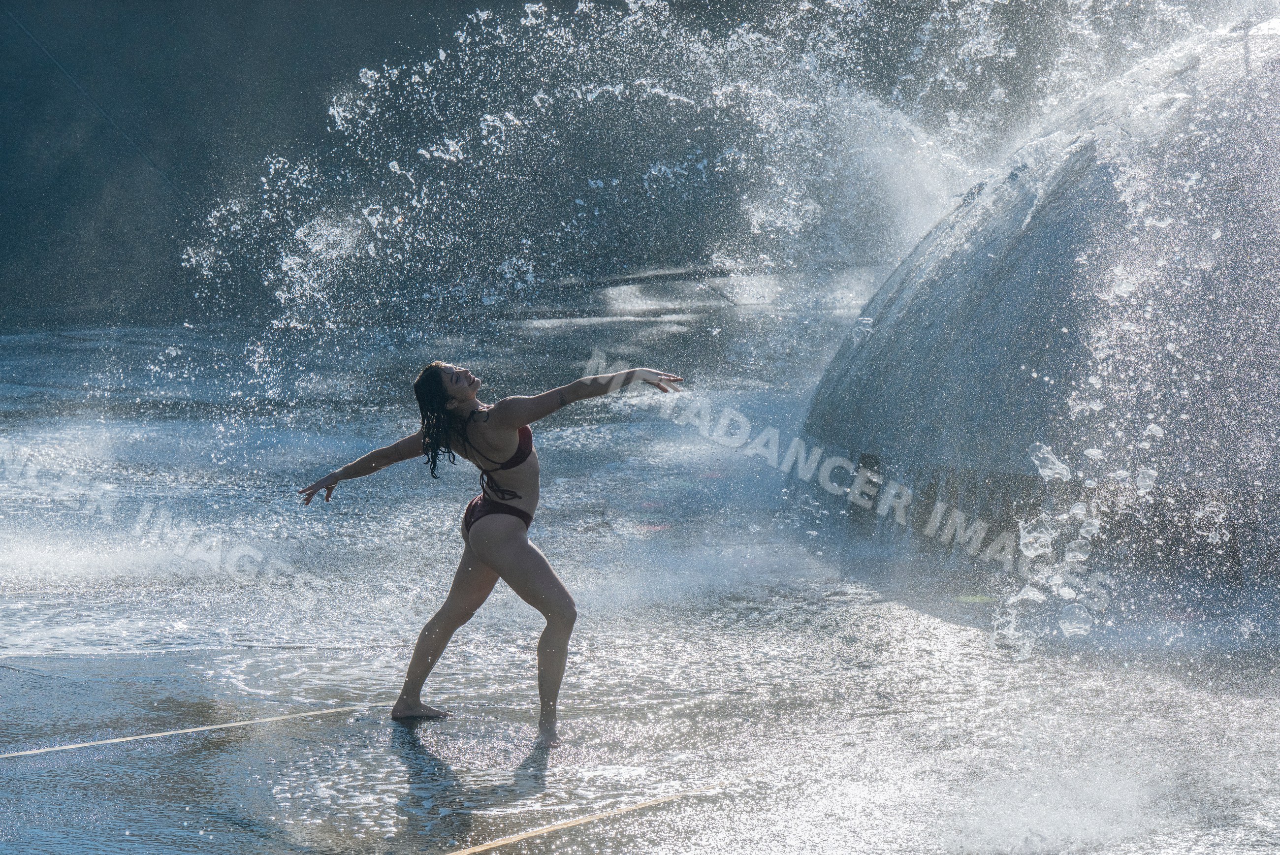 White woman dancing in swimsuit at a water fountain outdoors