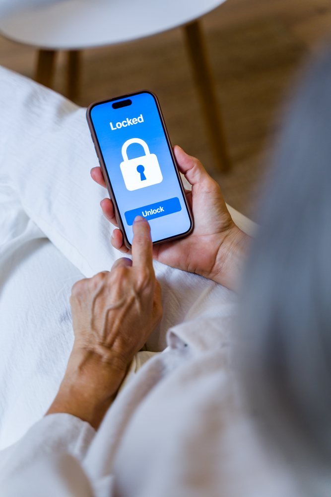 Hands unlocking a smartphone with locked screen on a bed indoors