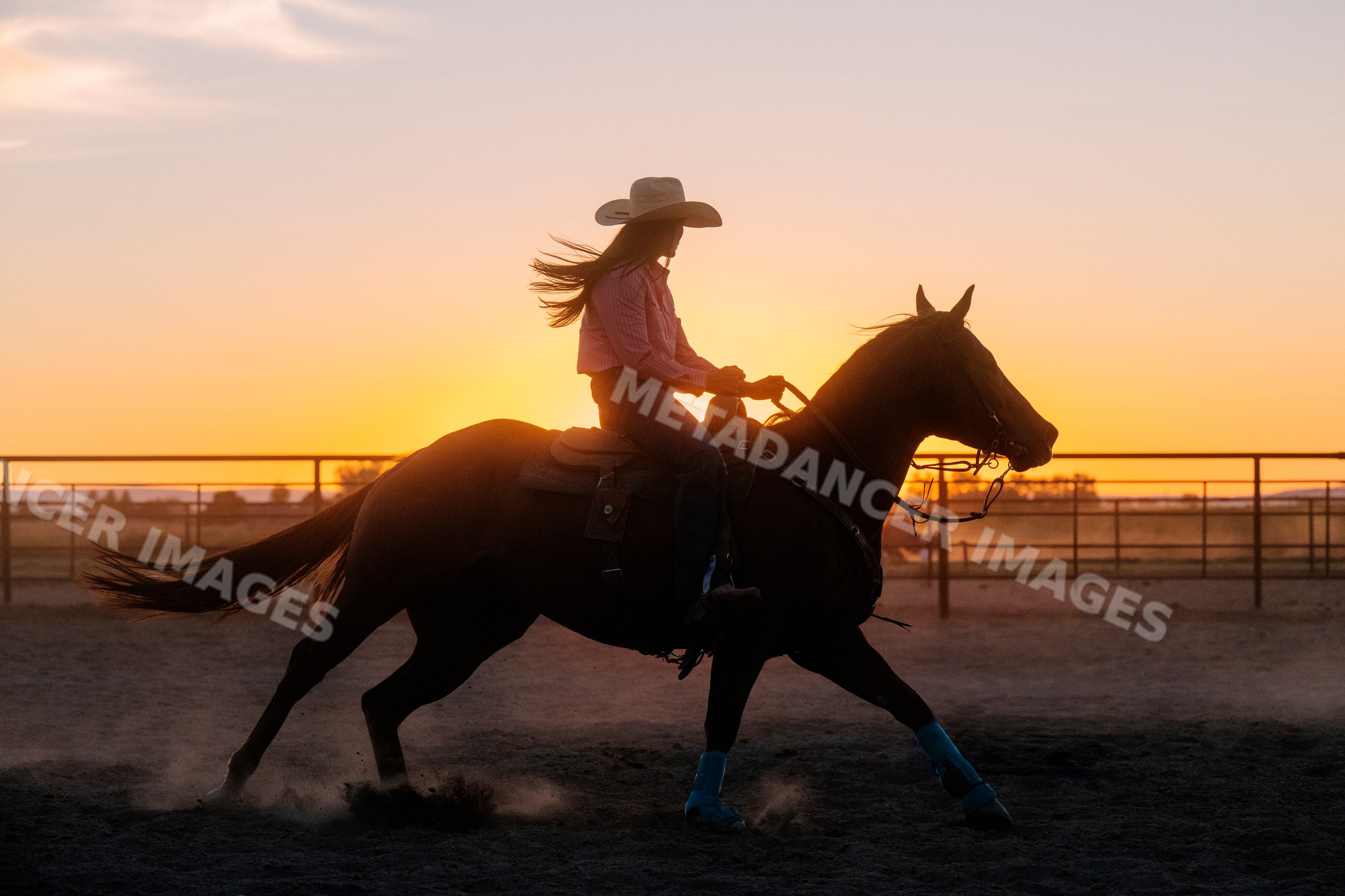 Horseback rider wearing cowboy hat at sunset in outdoor arena