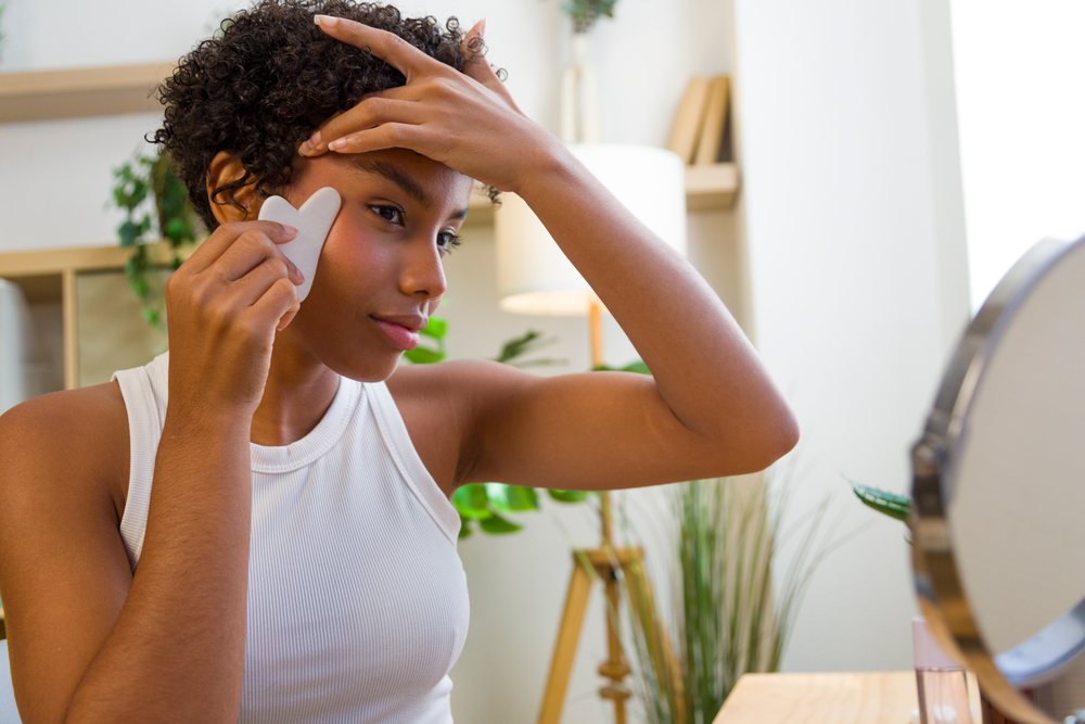 African American woman using gua sha tool for facial massage at home