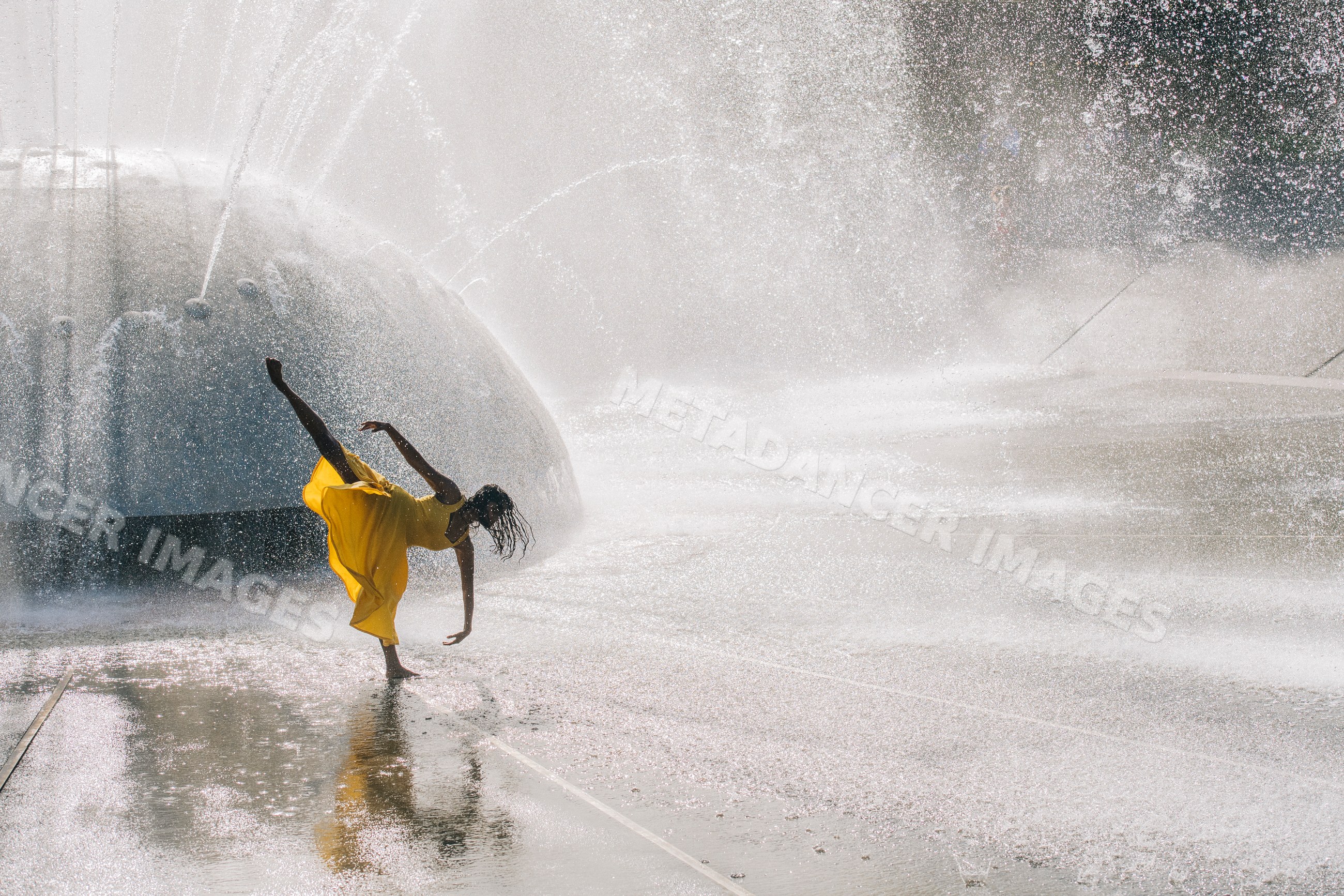 South Asian woman dancing in yellow dress at water fountain
