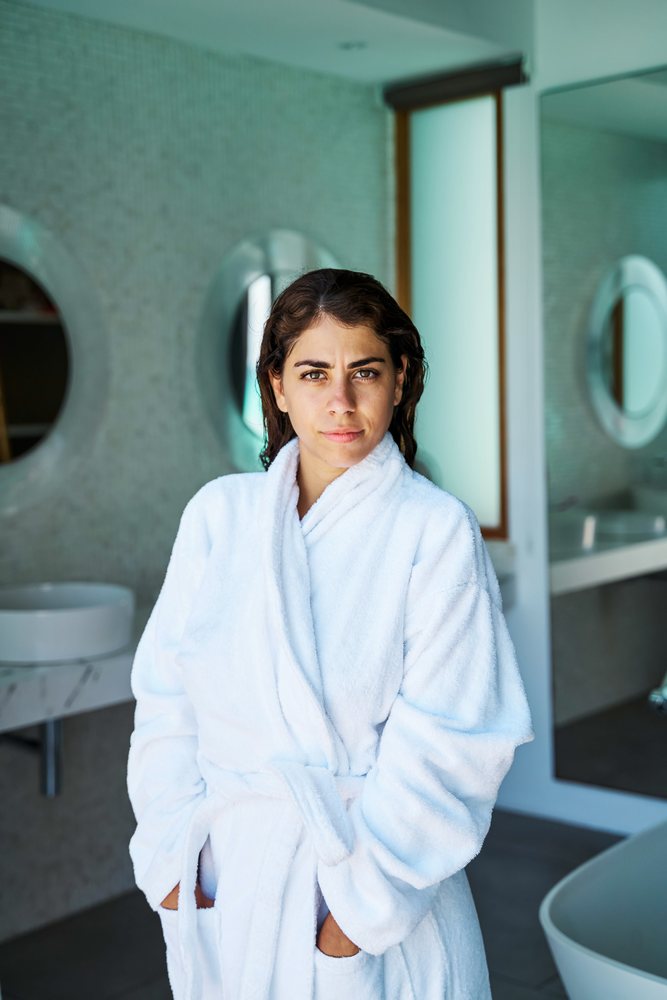 A woman in a white bathrobe stands in a modern bathroom