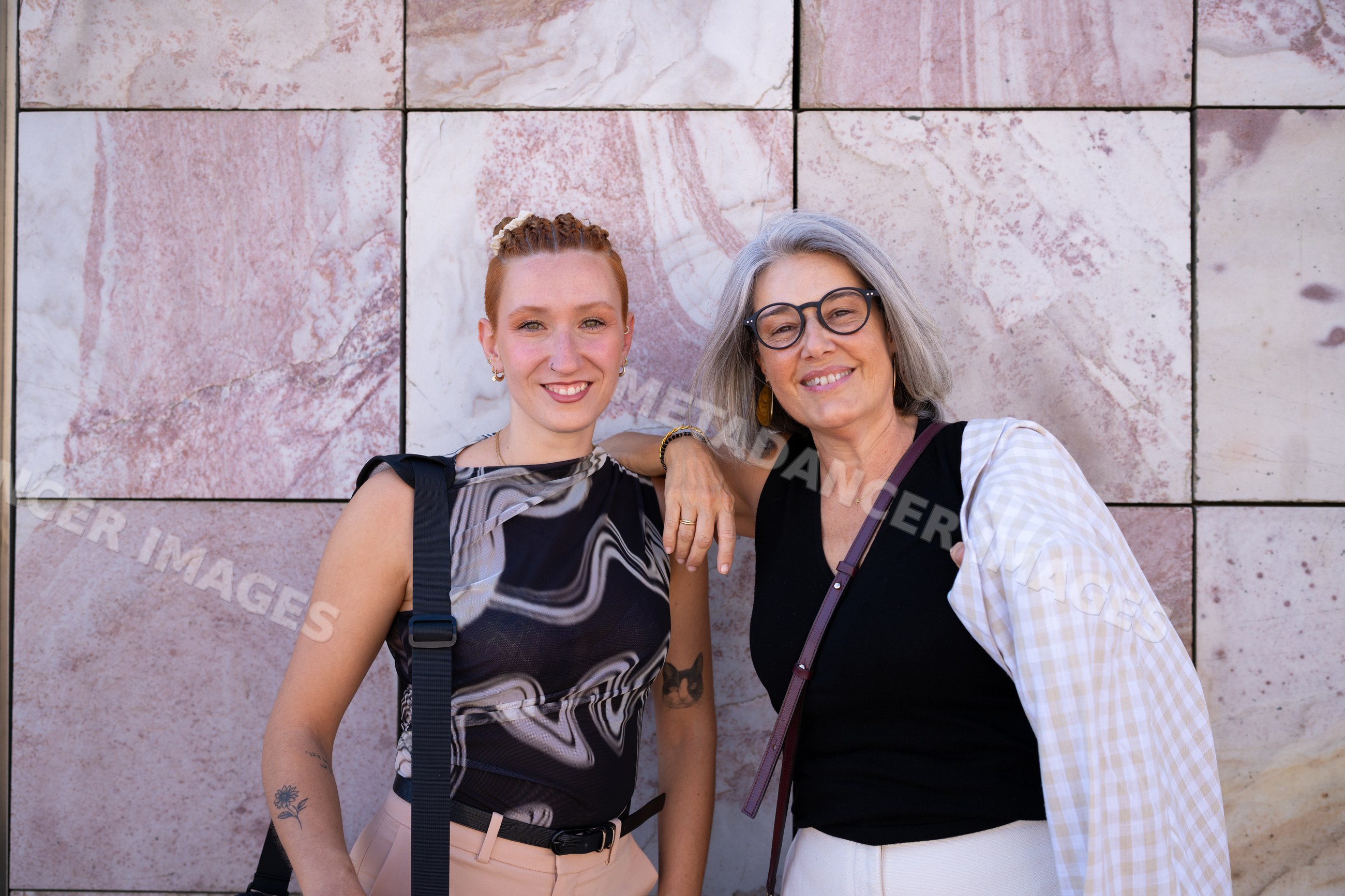 Two white women smiling and posing outdoors against marble wall