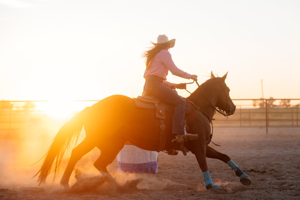 White woman riding horse in western riding arena at sunset