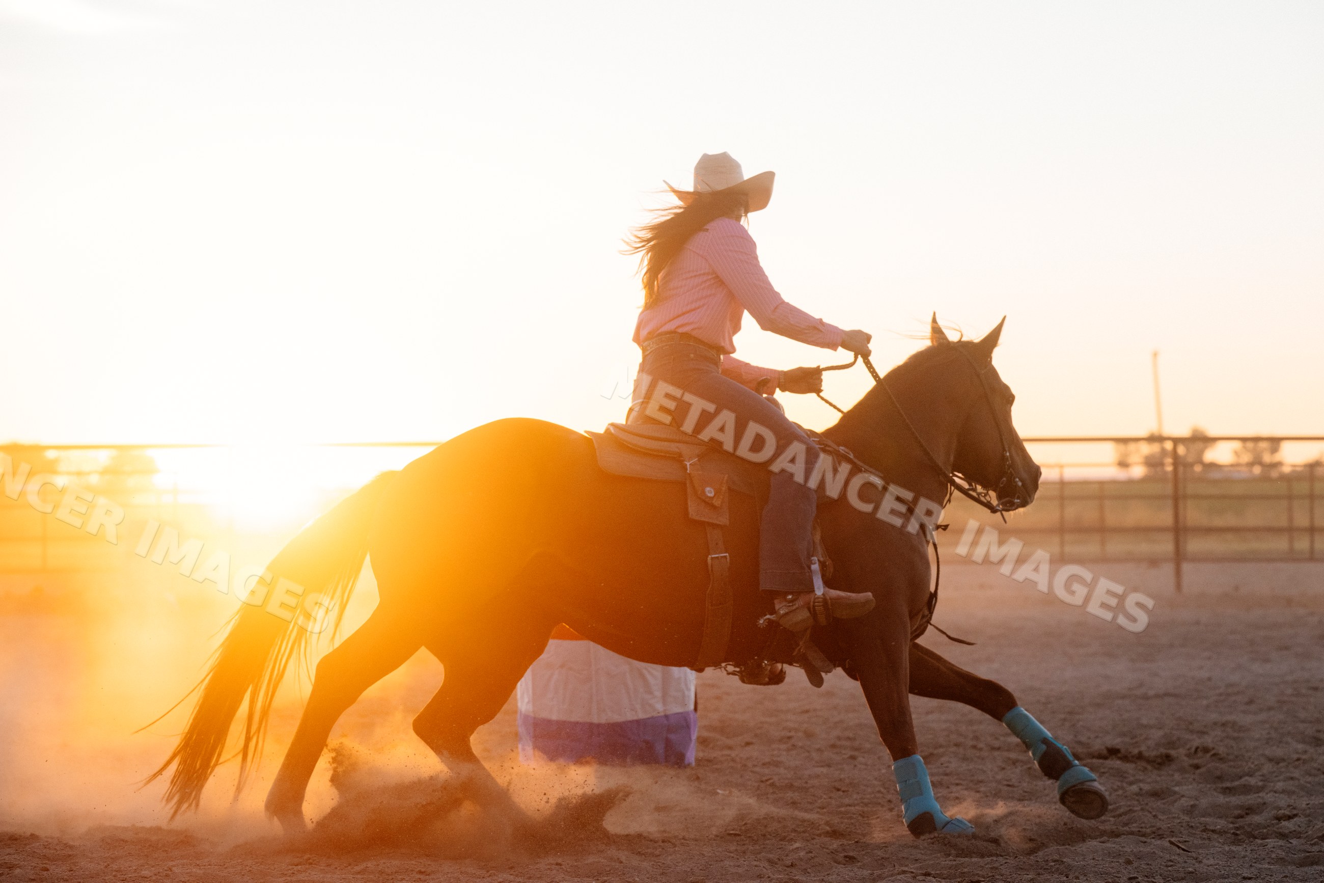 White woman riding horse in western riding arena at sunset