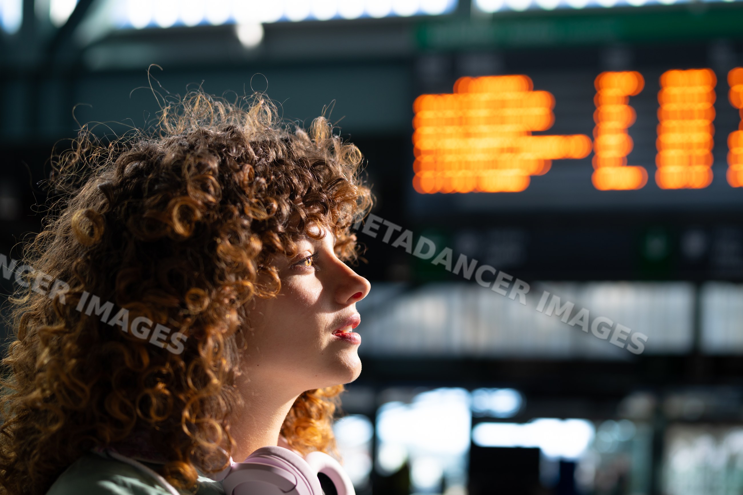 White woman with curly hair wearing headphones waiting