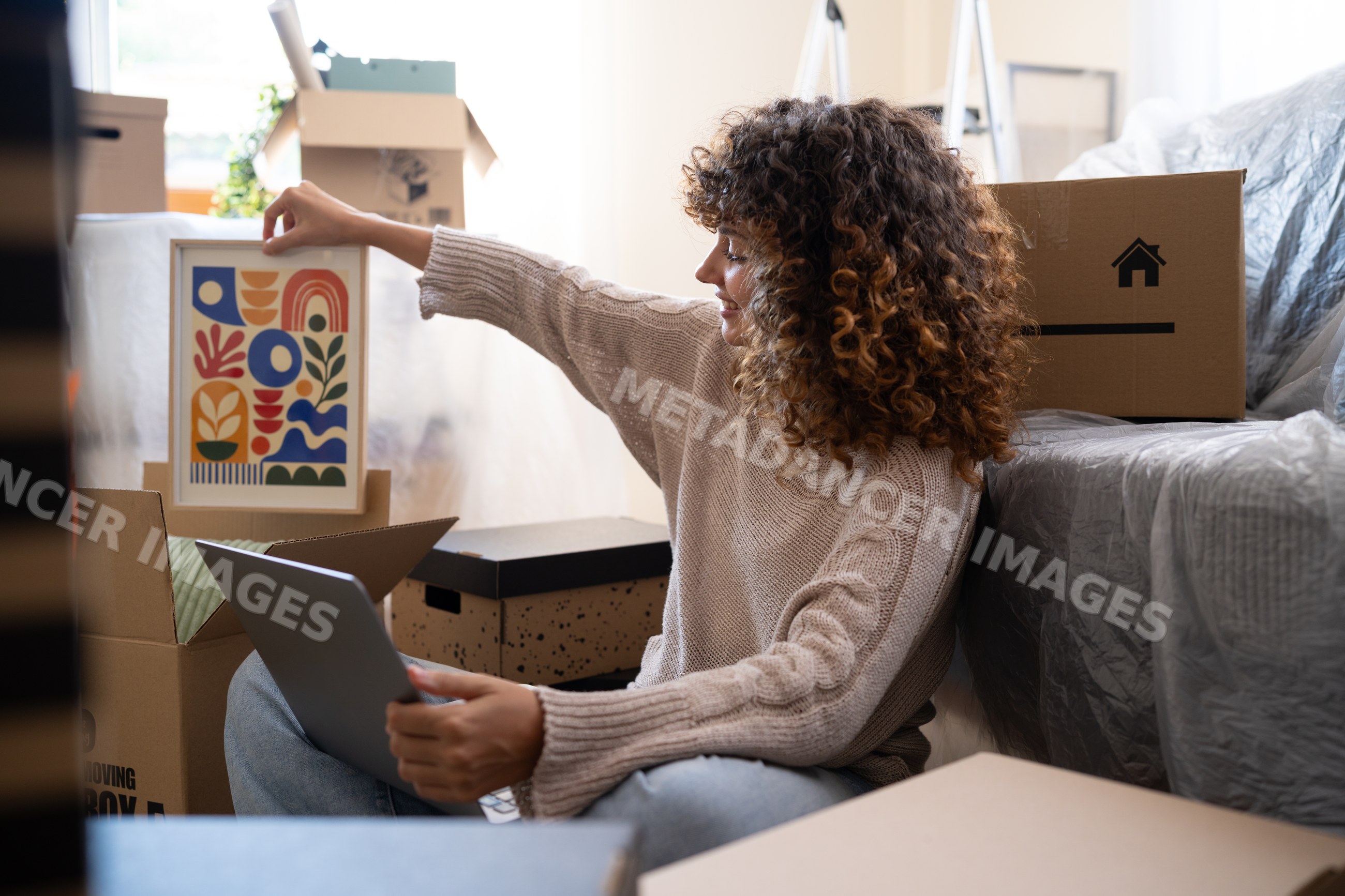 White woman unpacking framed abstract art among moving boxes indoors