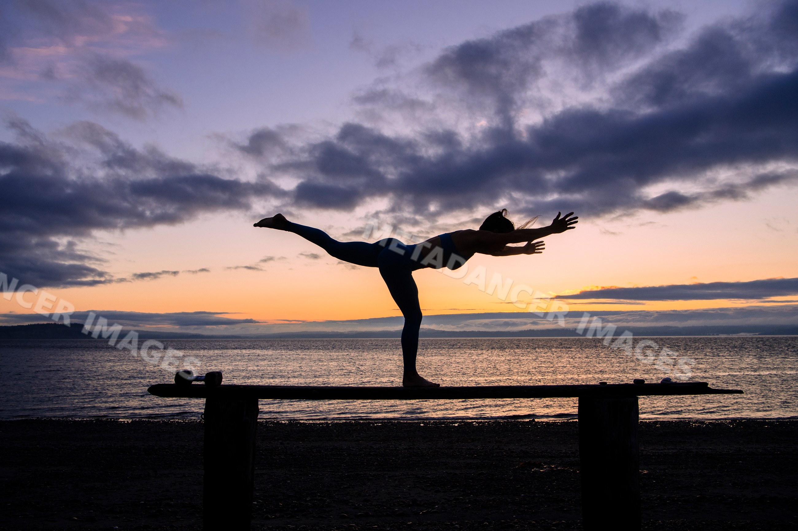 White woman practicing yoga balance pose on beach at sunset