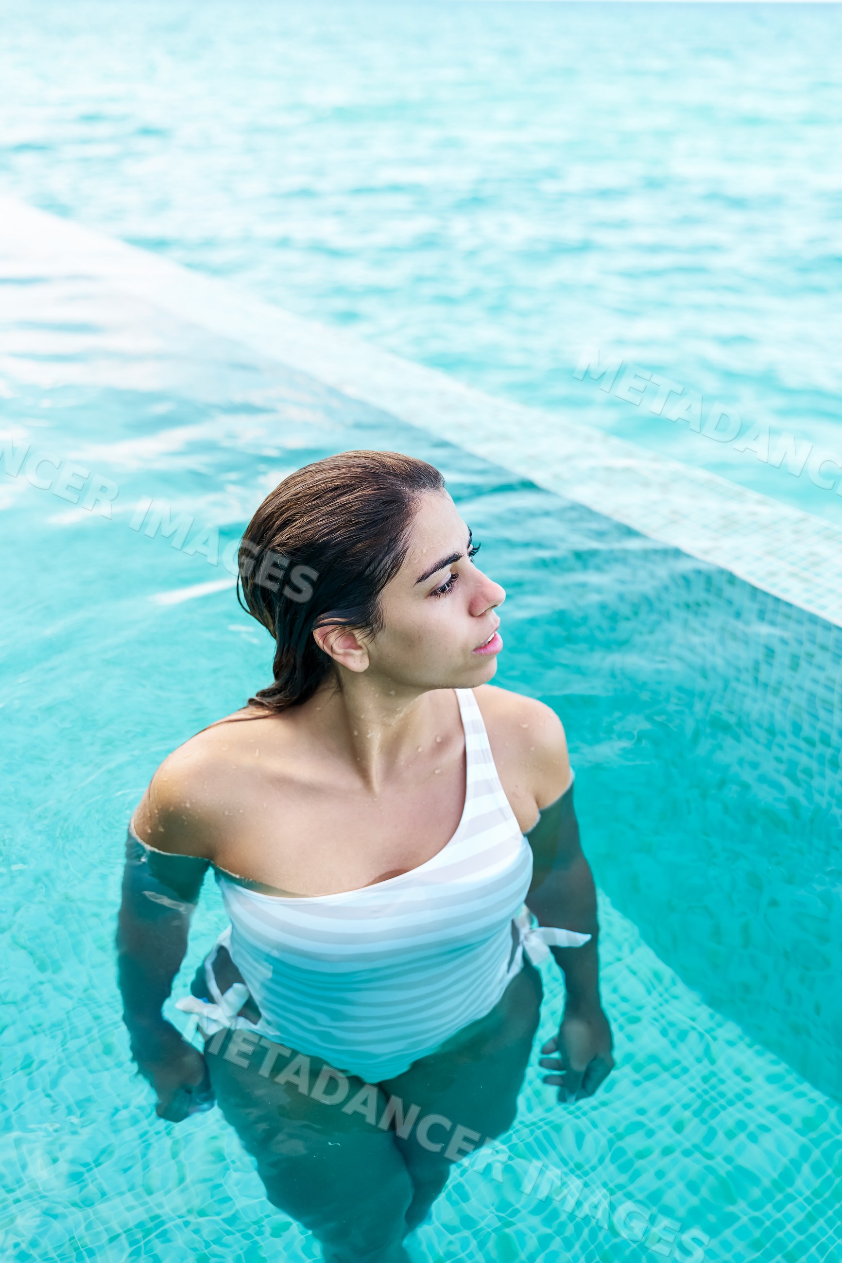 A white woman relaxes in a turquoise tiled swimming pool
