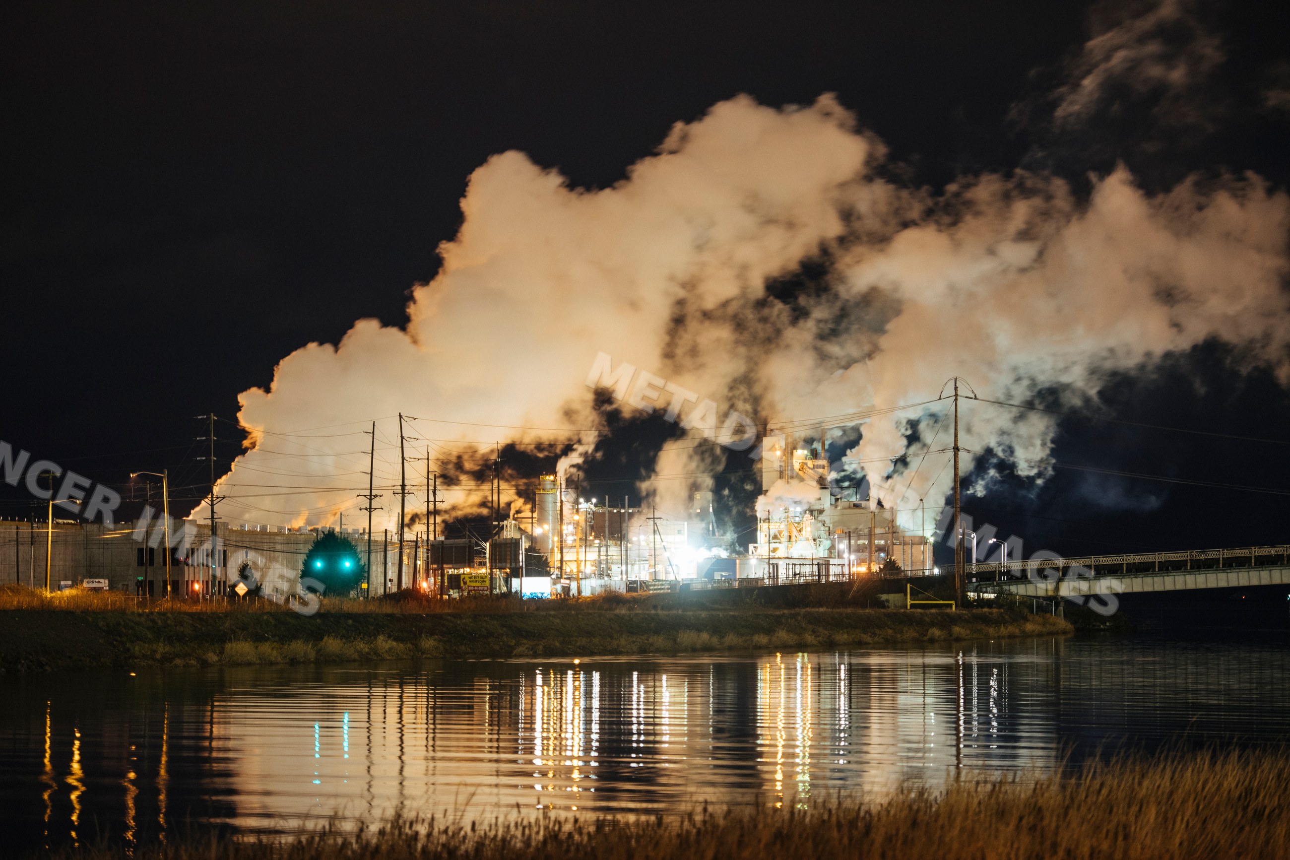 Industrial plant emitting smoke with water reflection at night