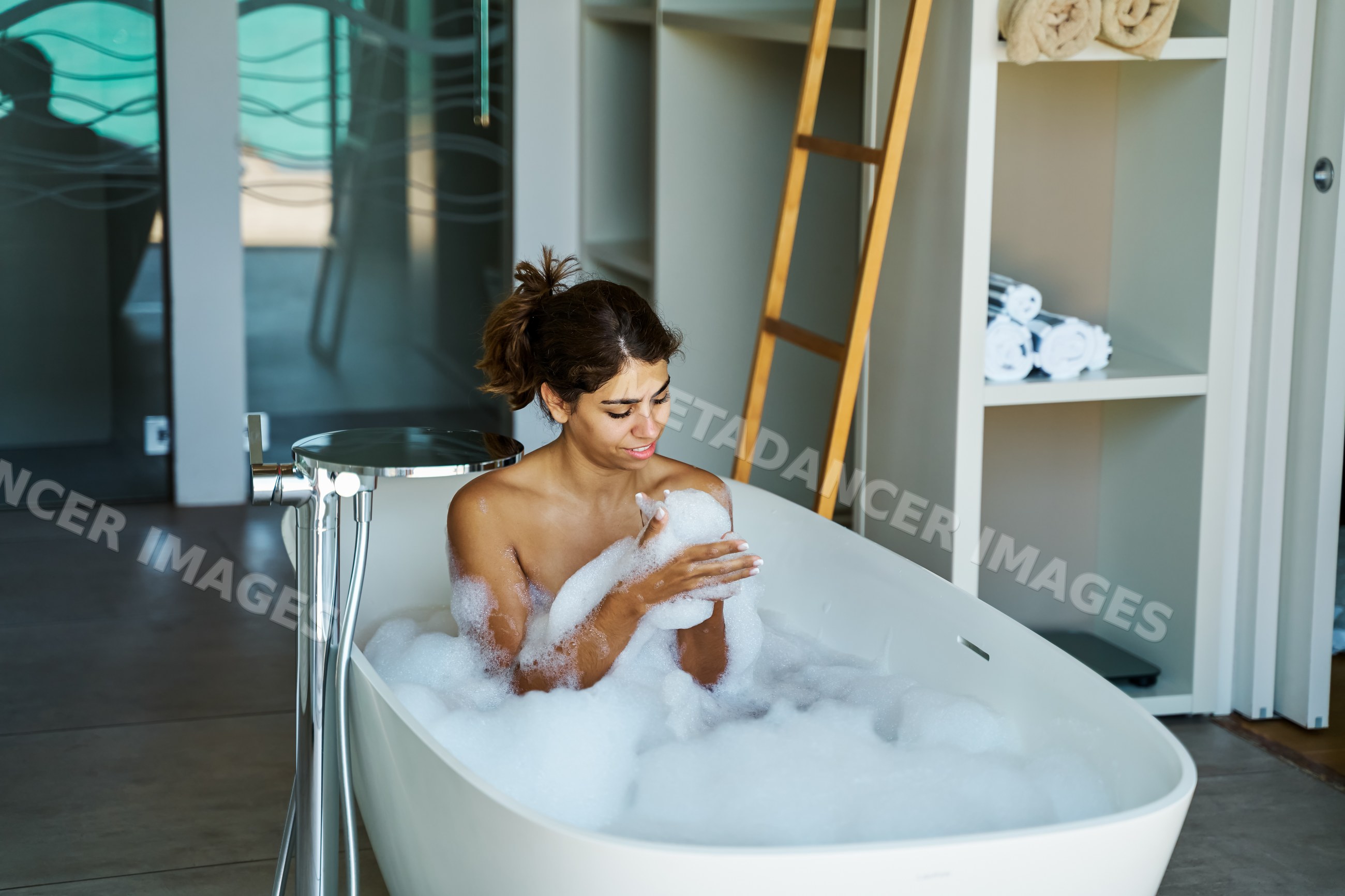 A white woman relaxes in a bubble bath in a modern bathroom