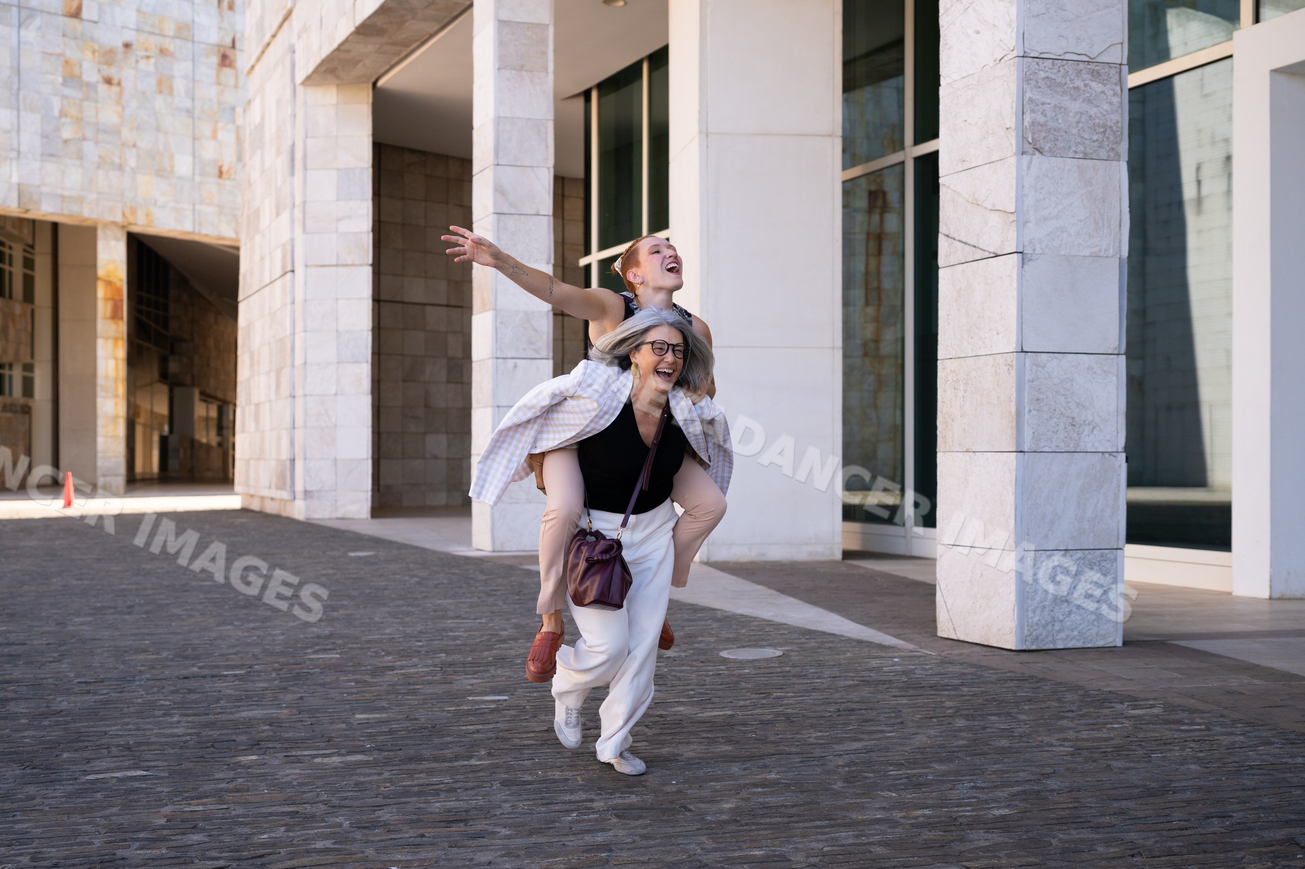 Two white women enjoying a playful piggyback ride in urban Spain