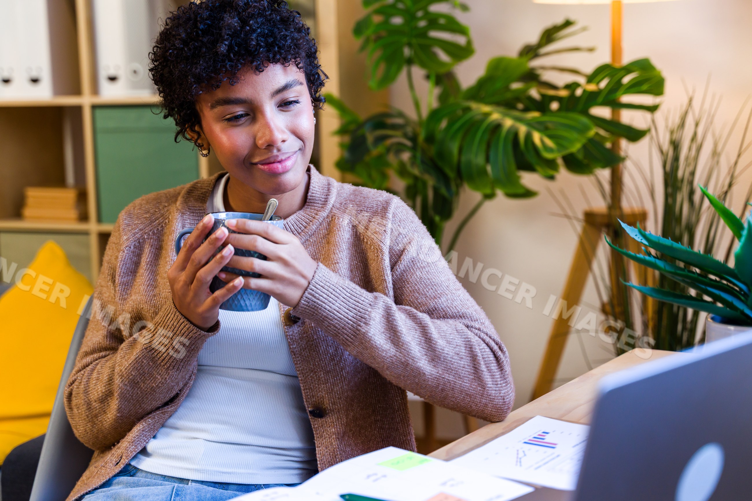 African American woman enjoying coffee at home office desk with plants