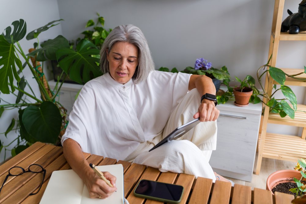 Mature white woman writing notes with tablet