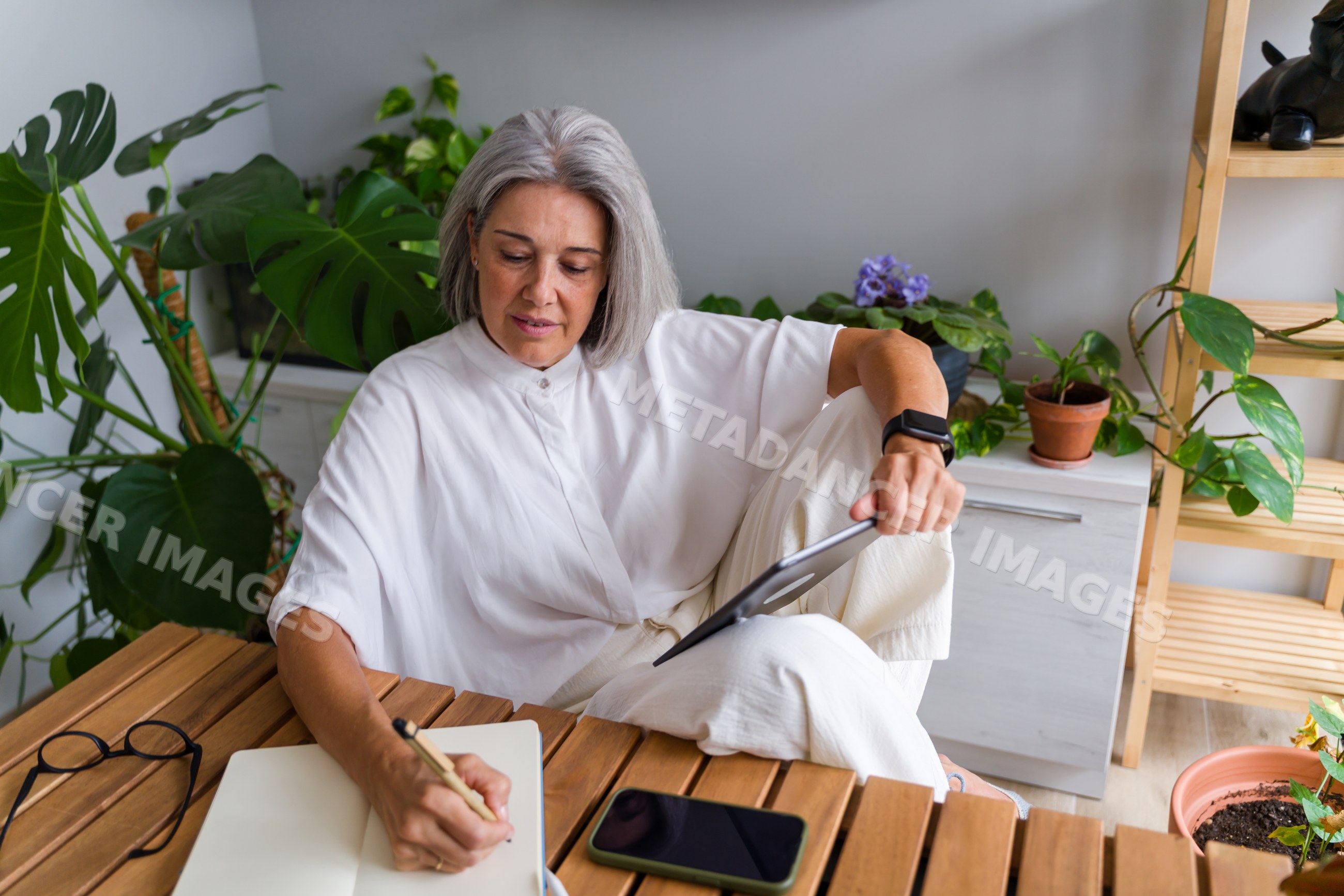 Mature white woman writing notes with tablet