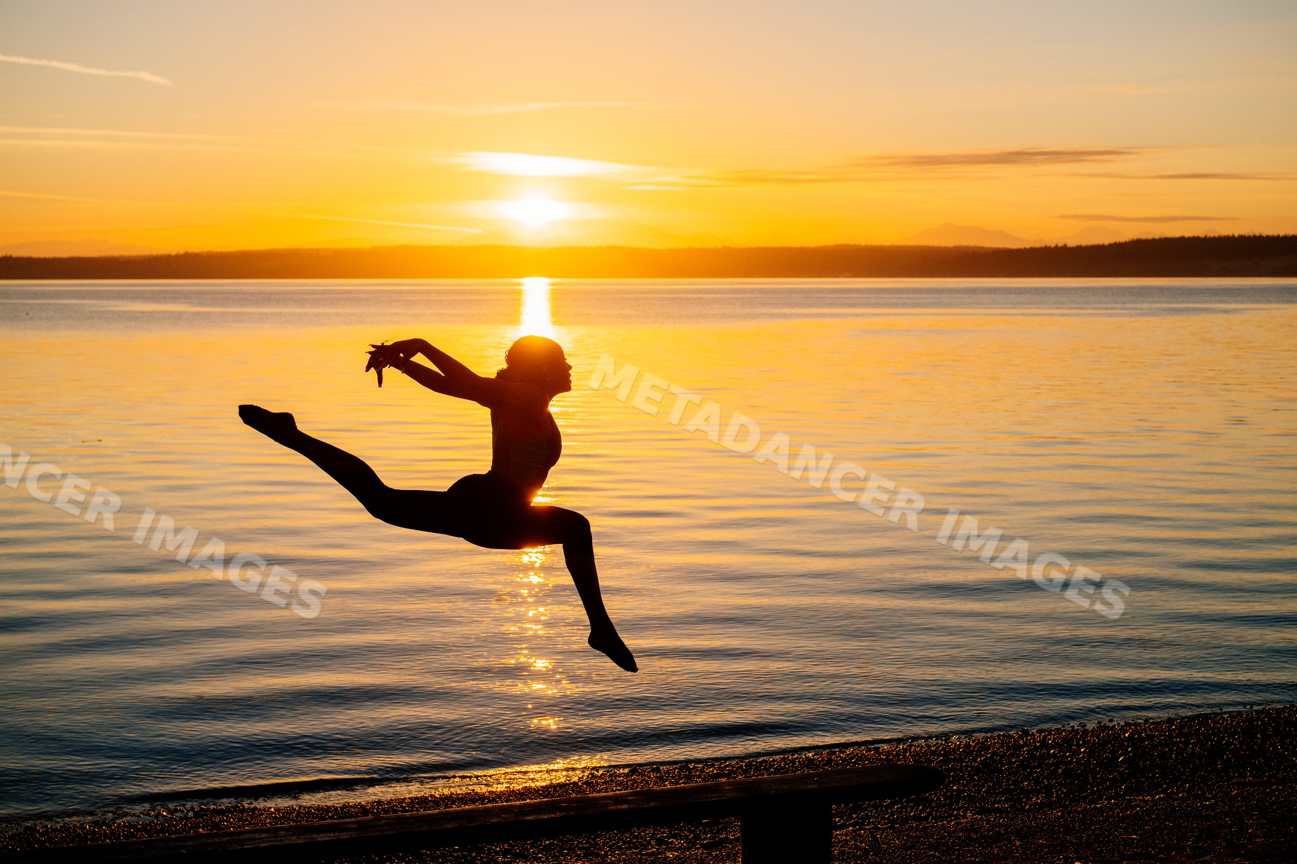 Silhouette of Hispanic woman leaping in yoga pose at lake sunset