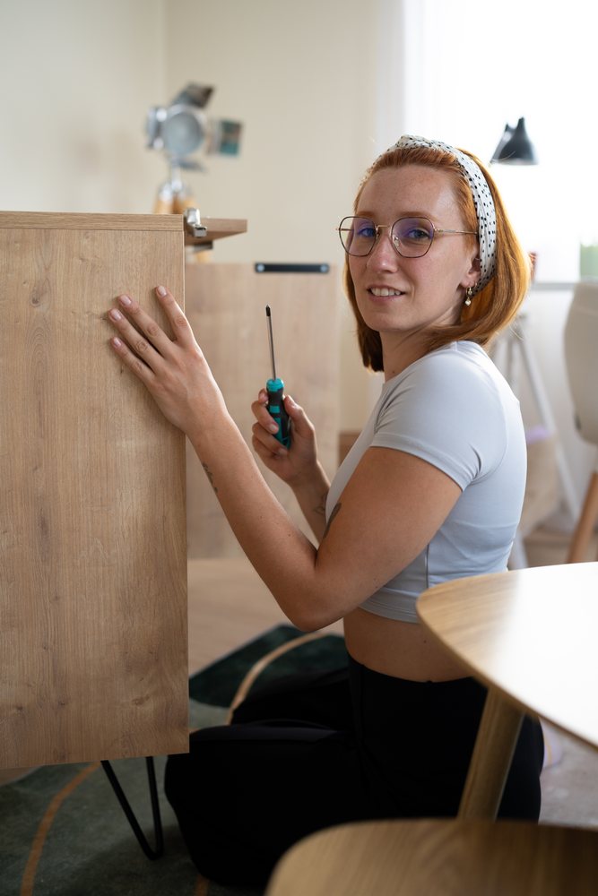 Young white woman assembling wooden furniture with screwdriver