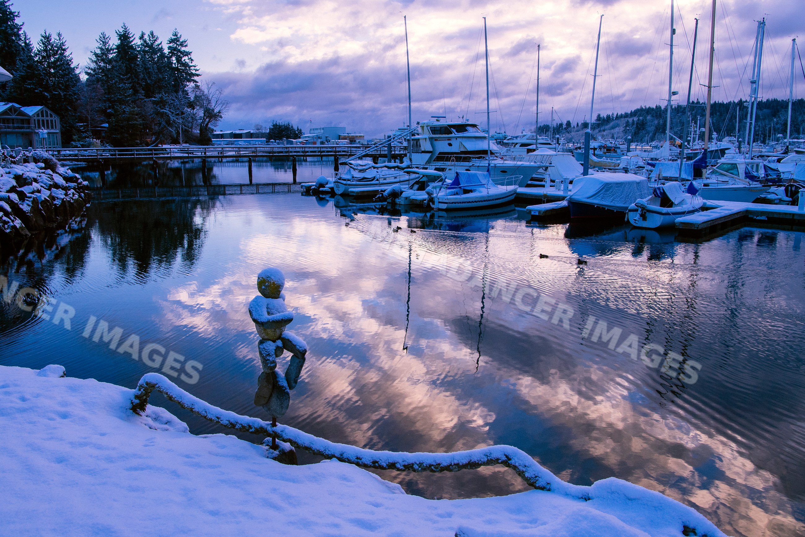 Marina with boats docked in winter snow reflecting clouds in water