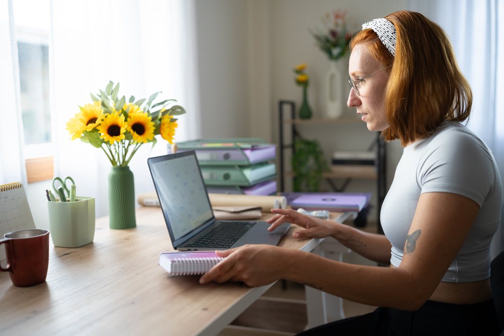 A white woman works on a laptop at a neat home office desk