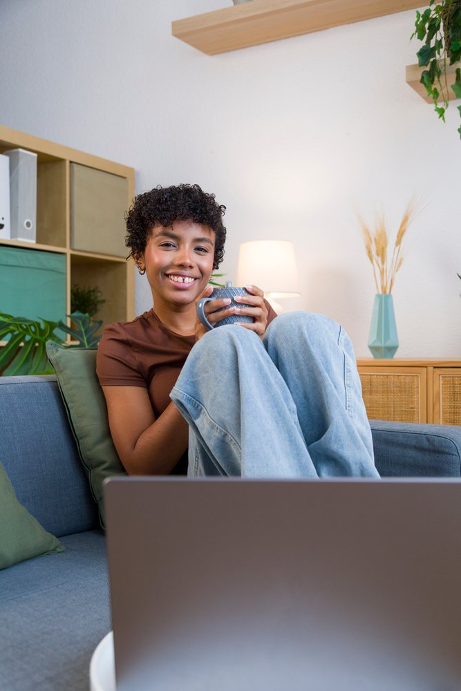 African American woman relaxing on blue sofa with cup and laptop