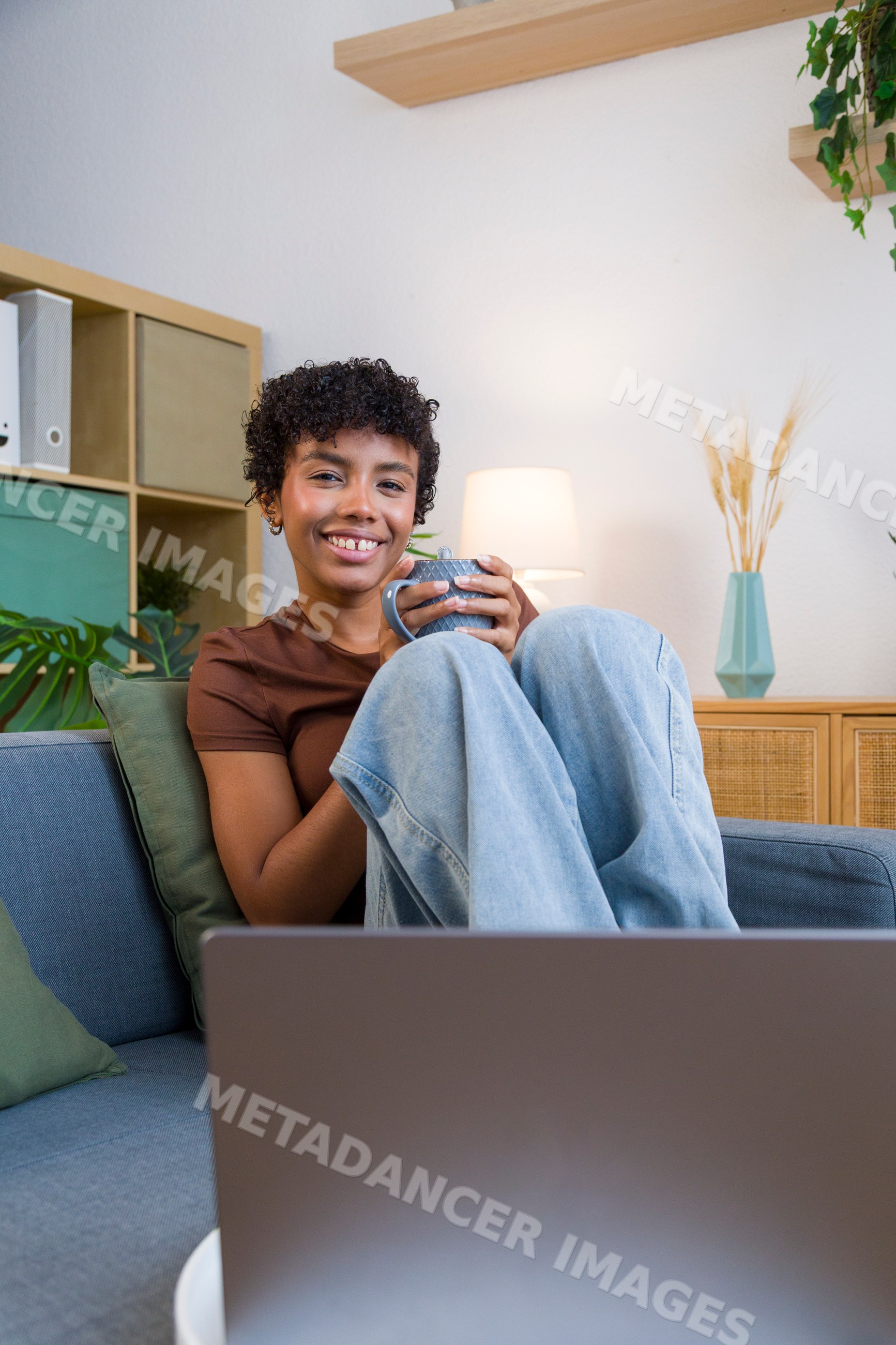 African American woman relaxing on blue sofa with cup and laptop