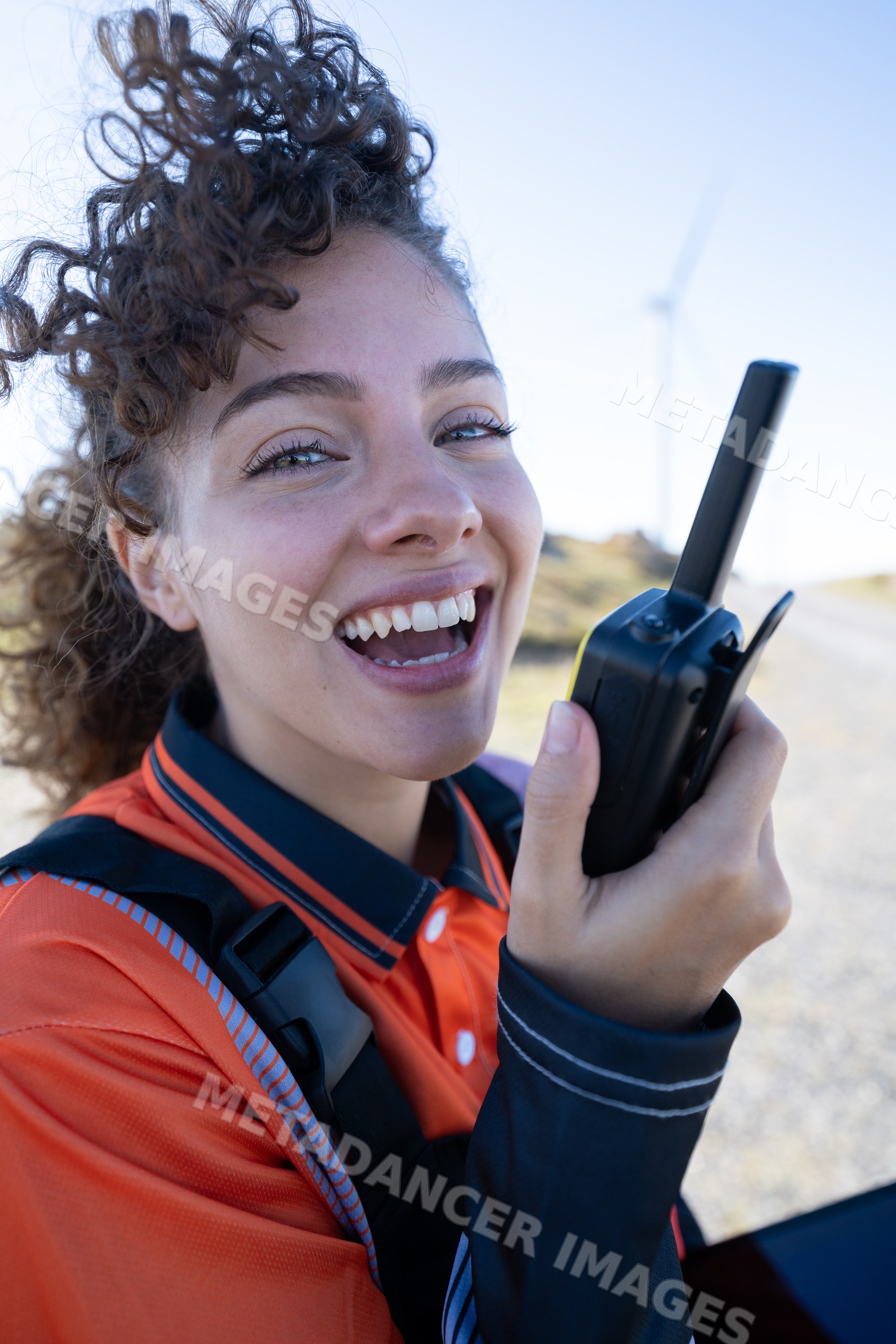 White woman holding walkie talkie near a wind turbine in Galicia