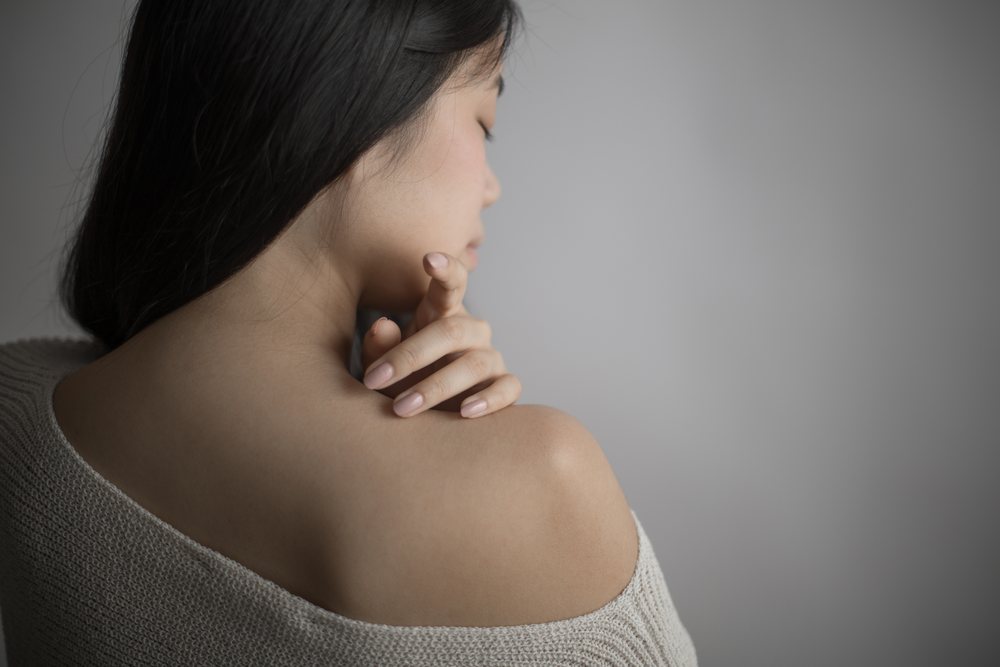 Southeast Asian woman touching shoulder in a thoughtful, peaceful pose
