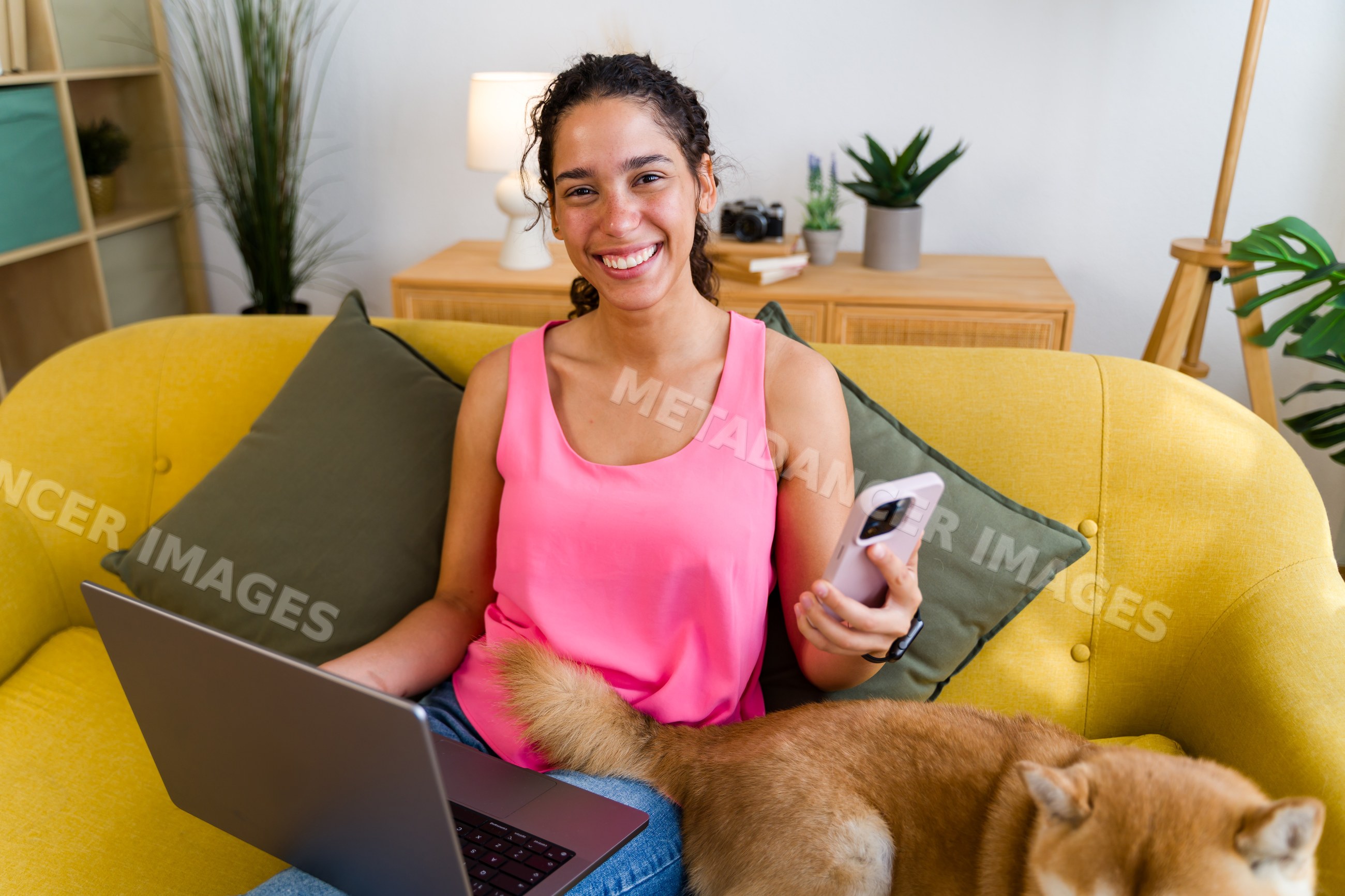 A Hispanic woman works on a laptop and holds a phone