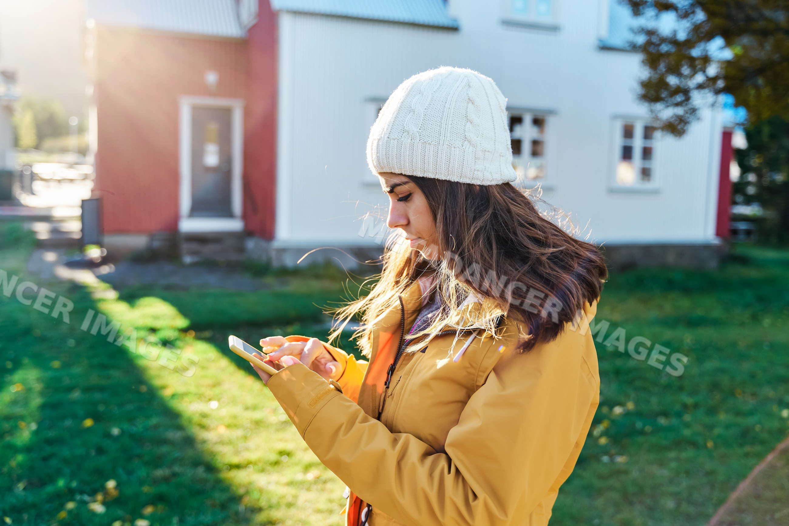 A white woman uses a smartphone outdoors in a yellow jacket