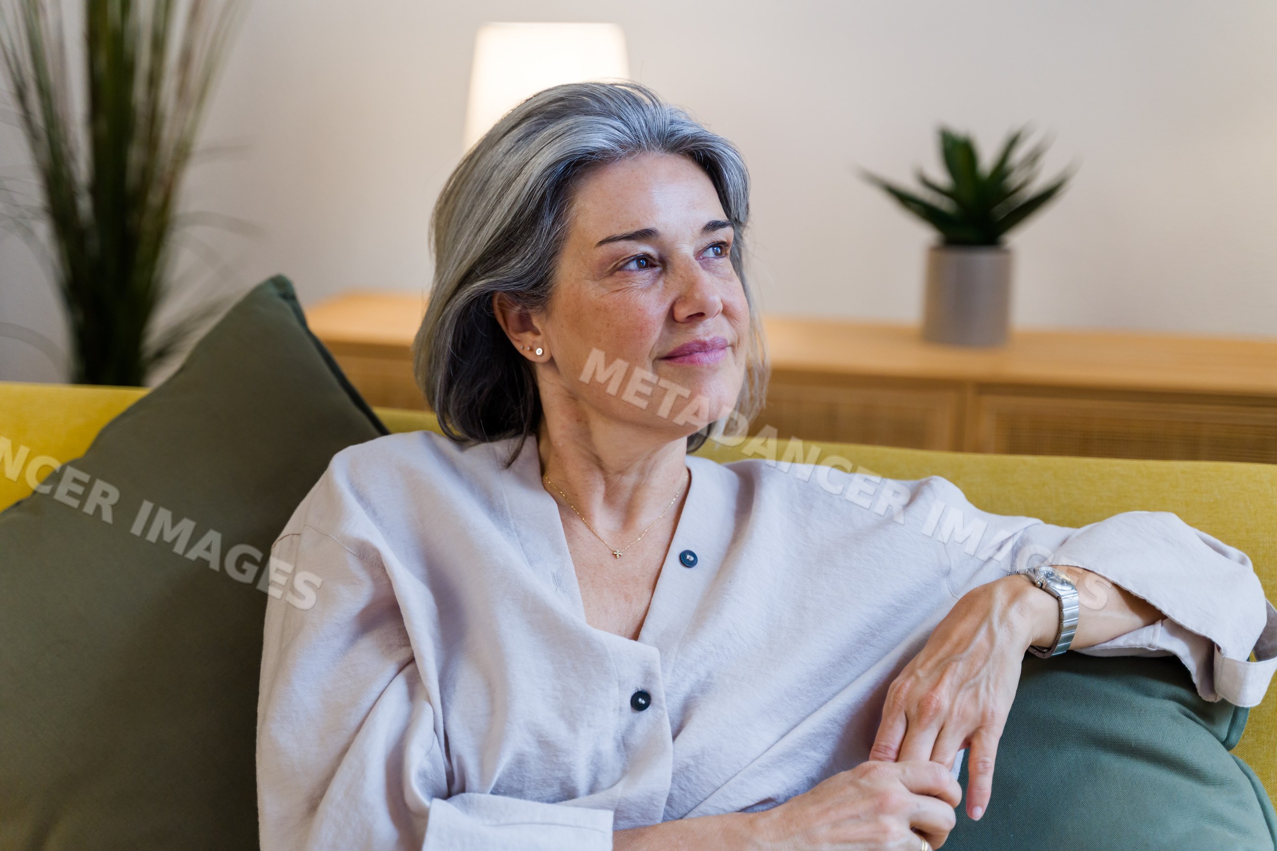 Thoughtful white woman sitting on yellow sofa in living room