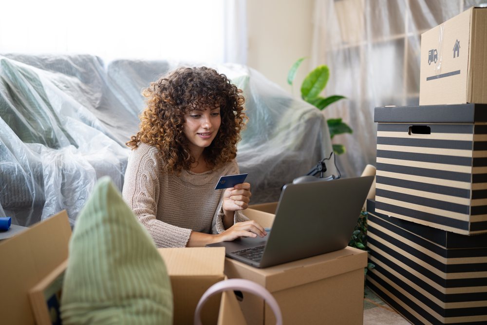 White woman shopping online using credit card during home move