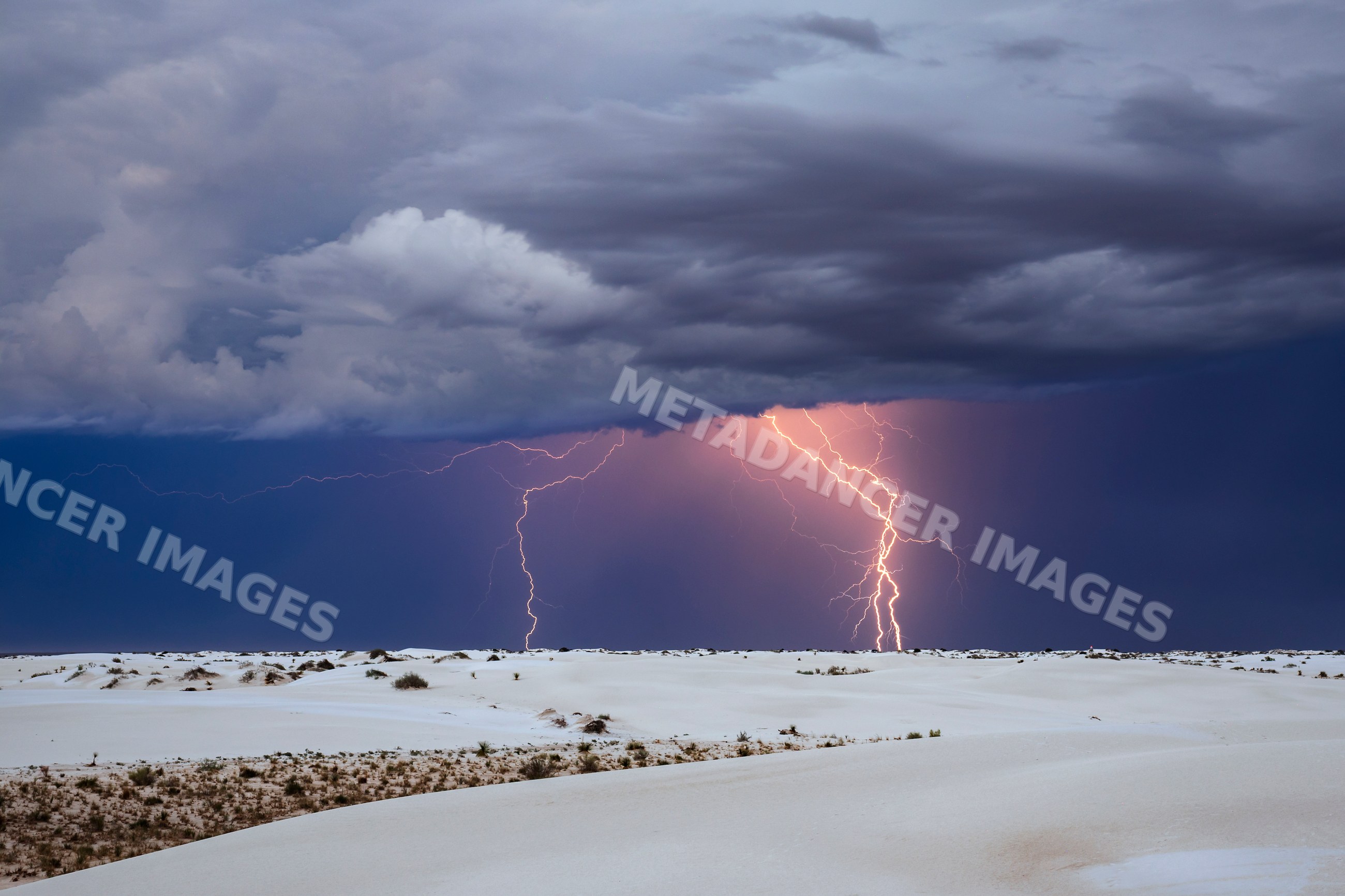 Lightning strikes over white sand dunes in a park
