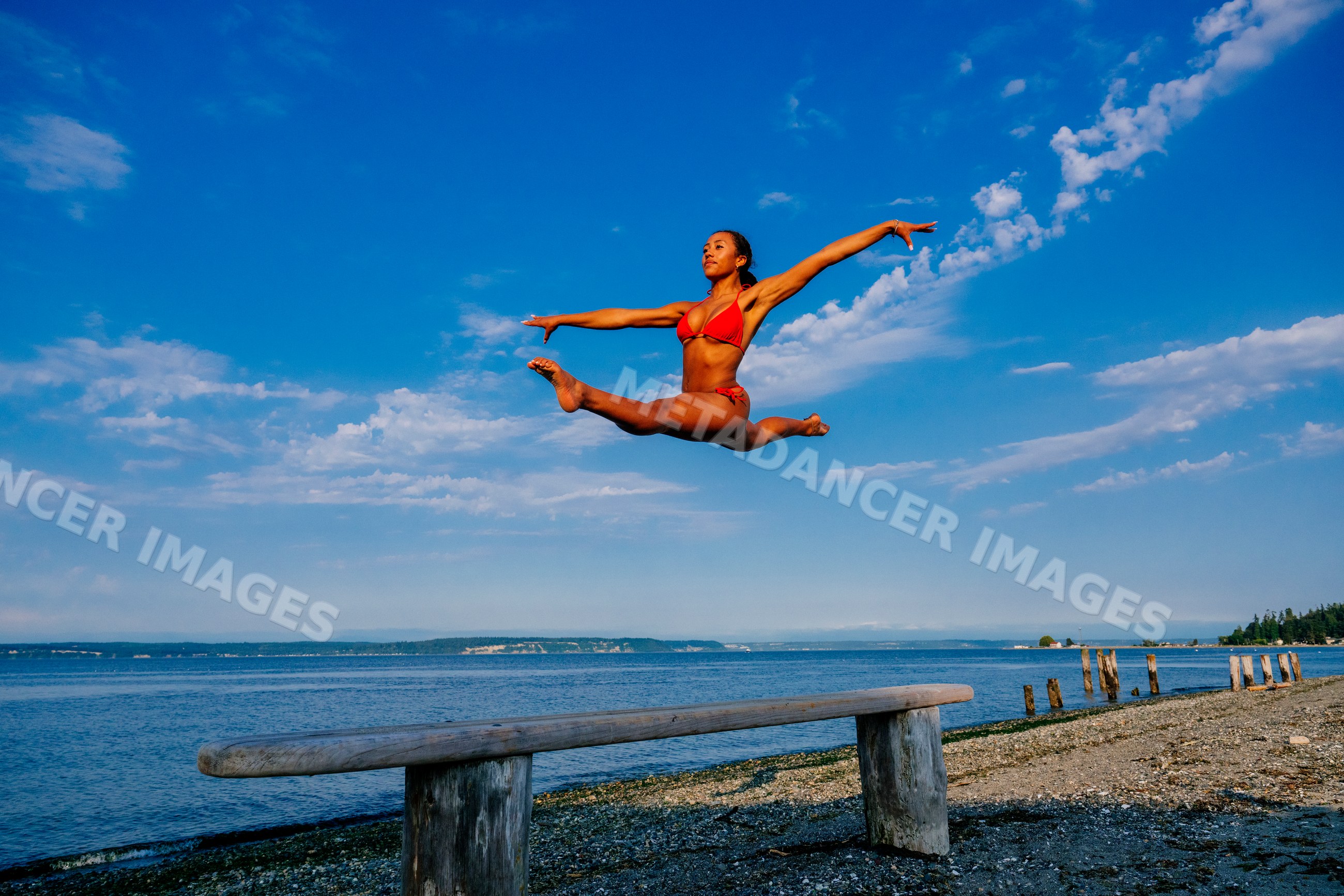Woman in red swimsuit jumping in a split leap on a beach in WA, USA
