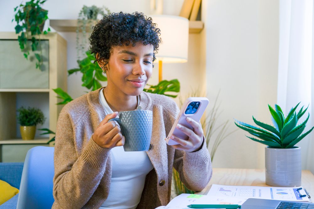 African American woman drinking from a mug and using smartphone
