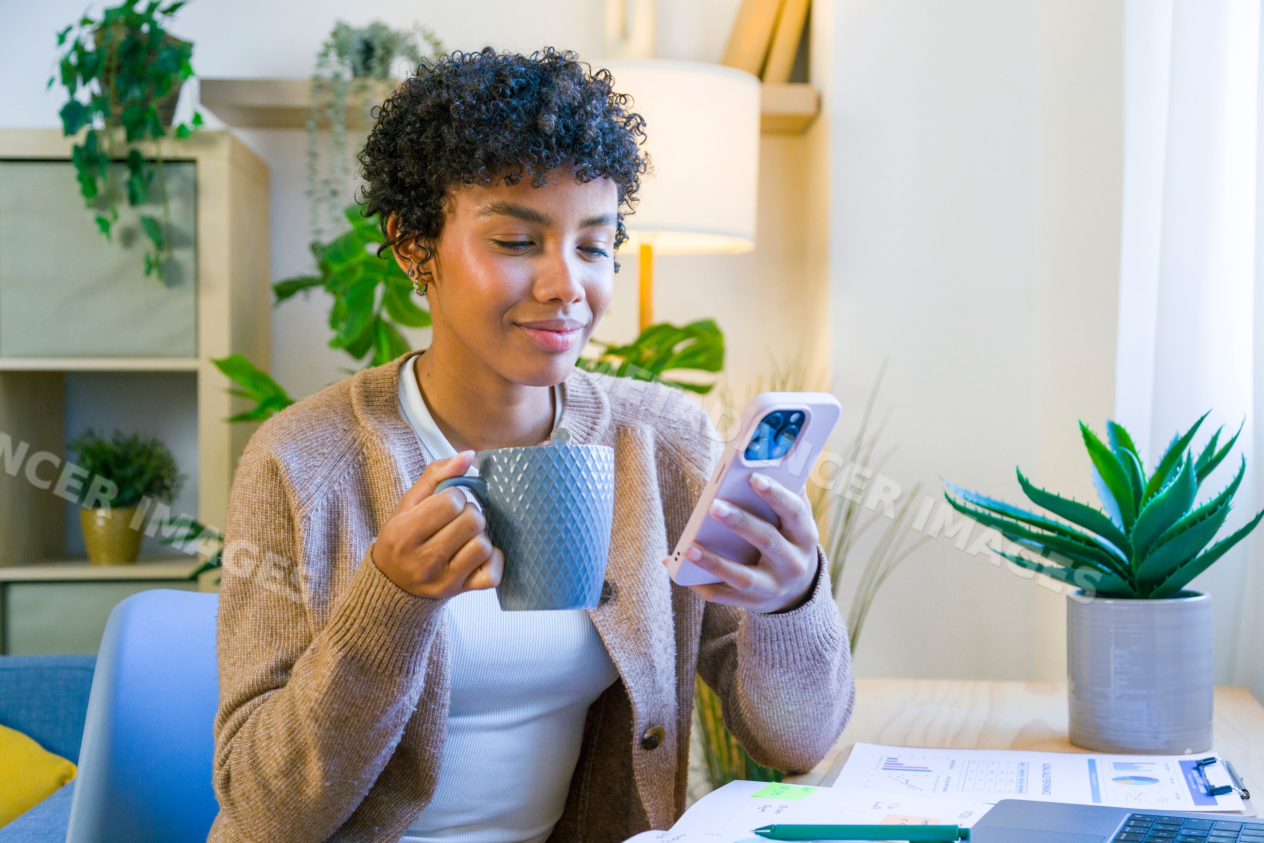 African American woman drinking from a mug and using smartphone