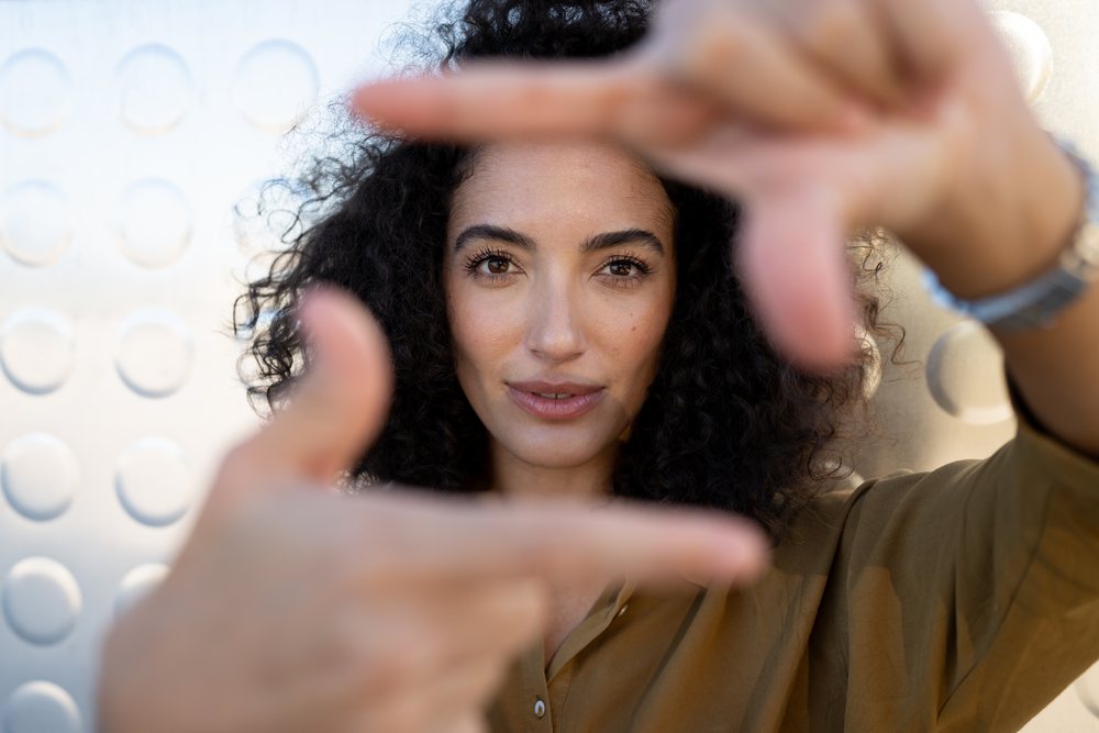 Woman framing face with hands outdoors in thoughtful gesture