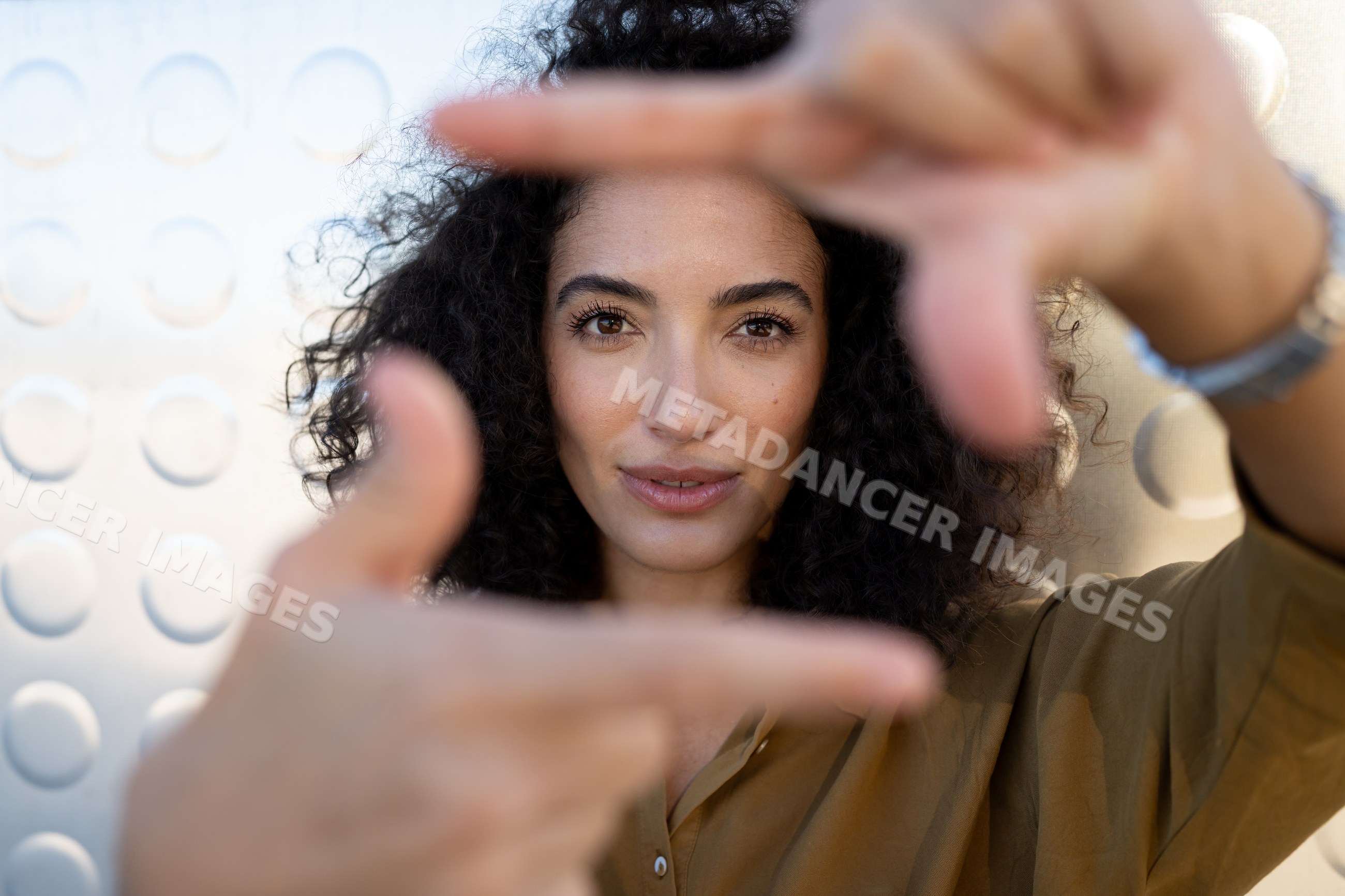 Woman framing face with hands outdoors in thoughtful gesture