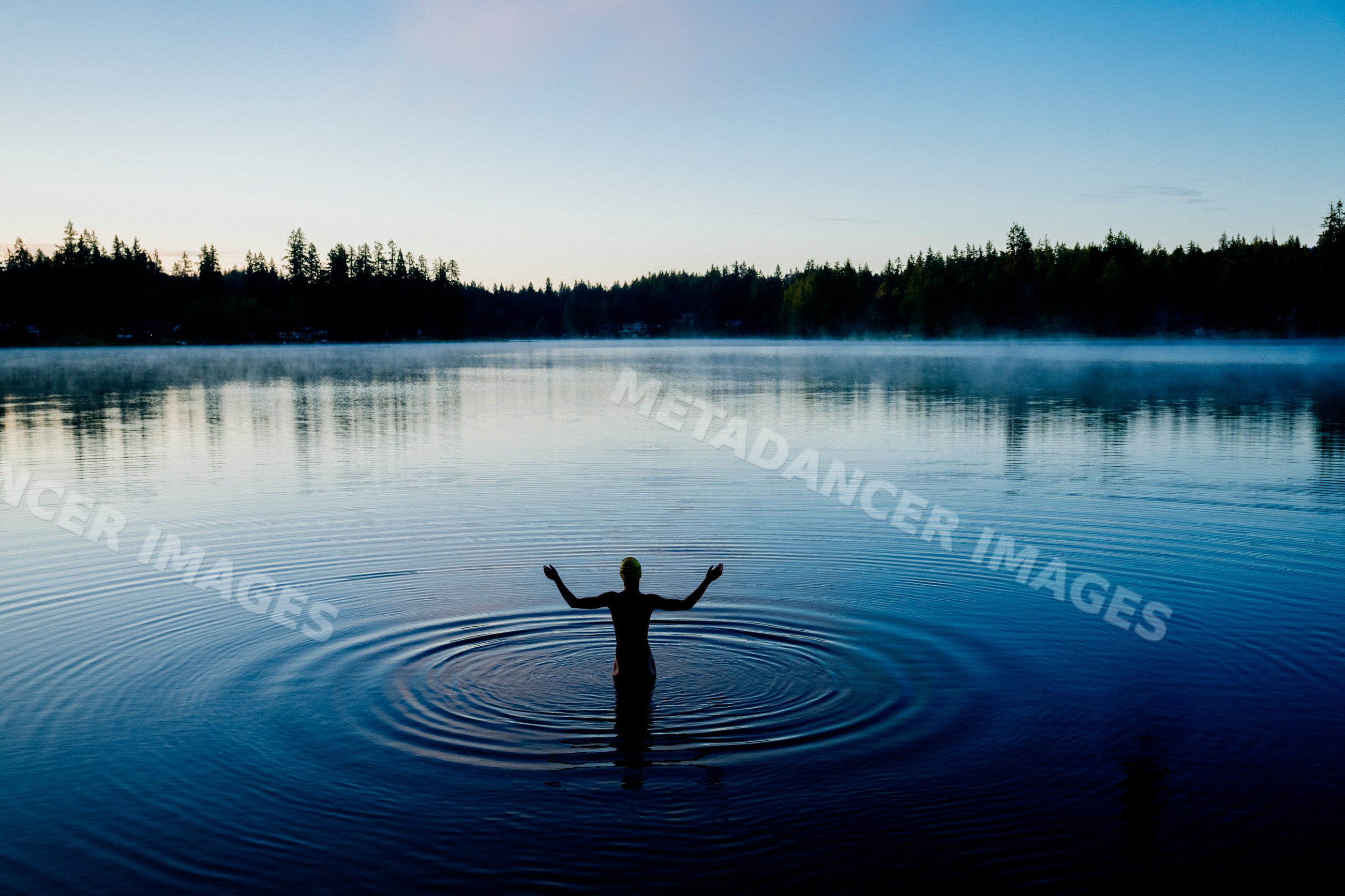 White person standing in calm lake water with ripples at misty forest