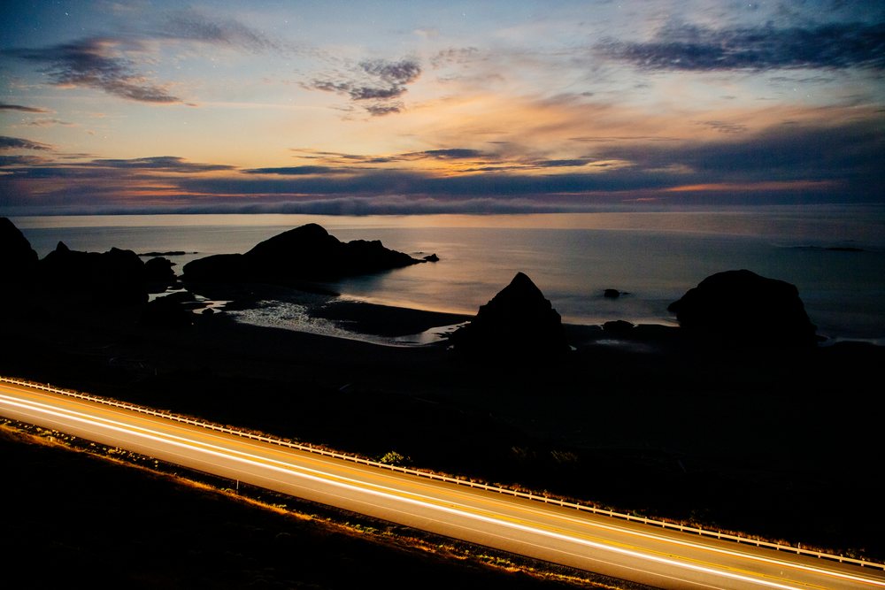 Highway light trails along rocky coastline at sunset in Oregon