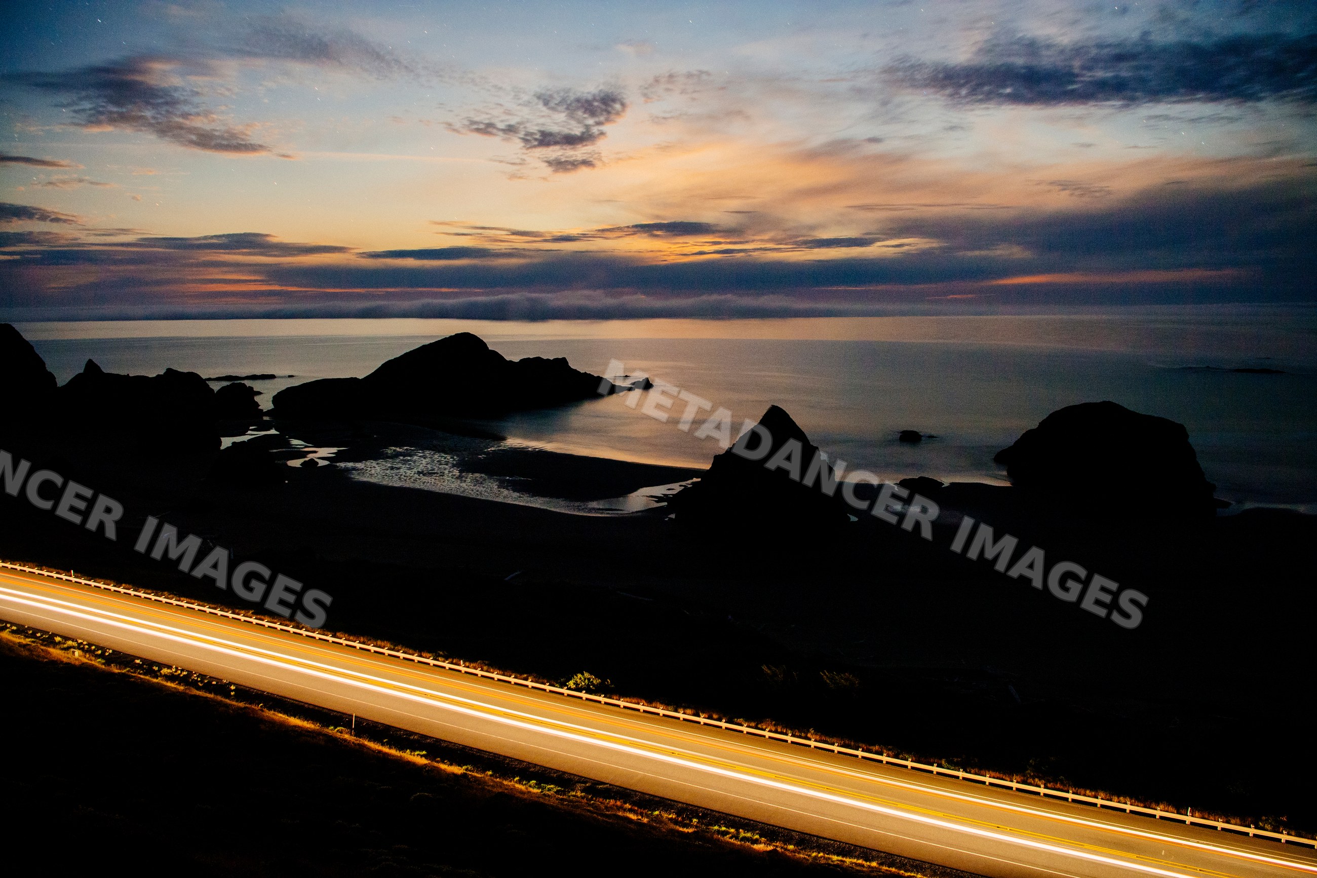 Highway light trails along rocky coastline at sunset in Oregon