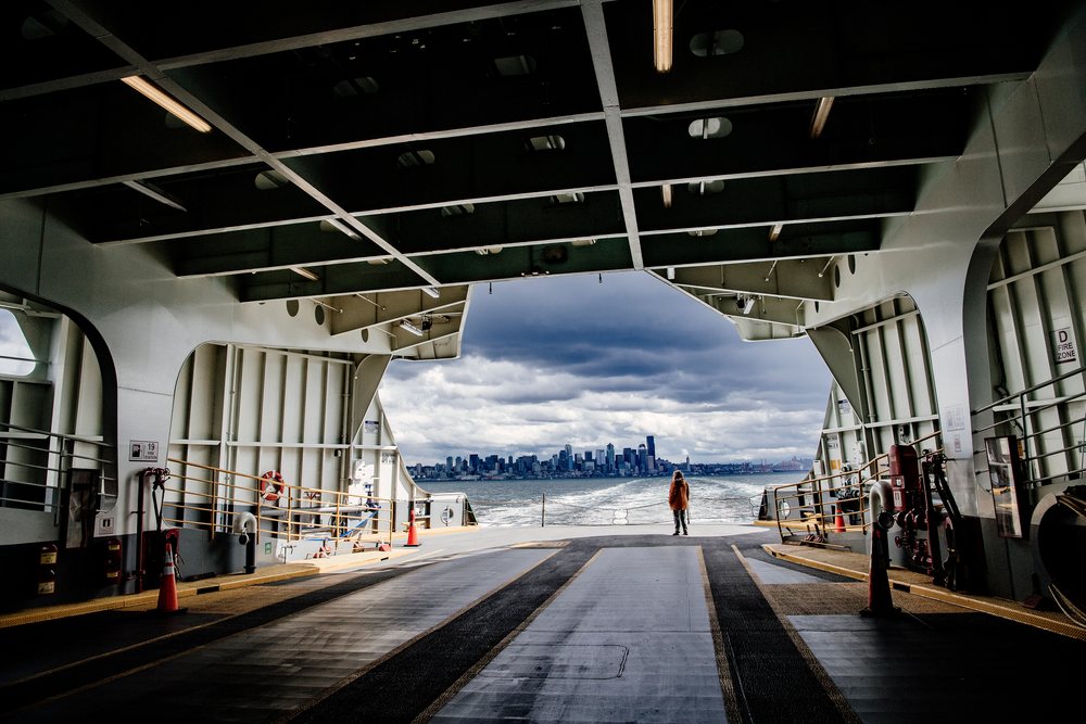 Person stands on a ferry deck viewing a city skyline on an overcast