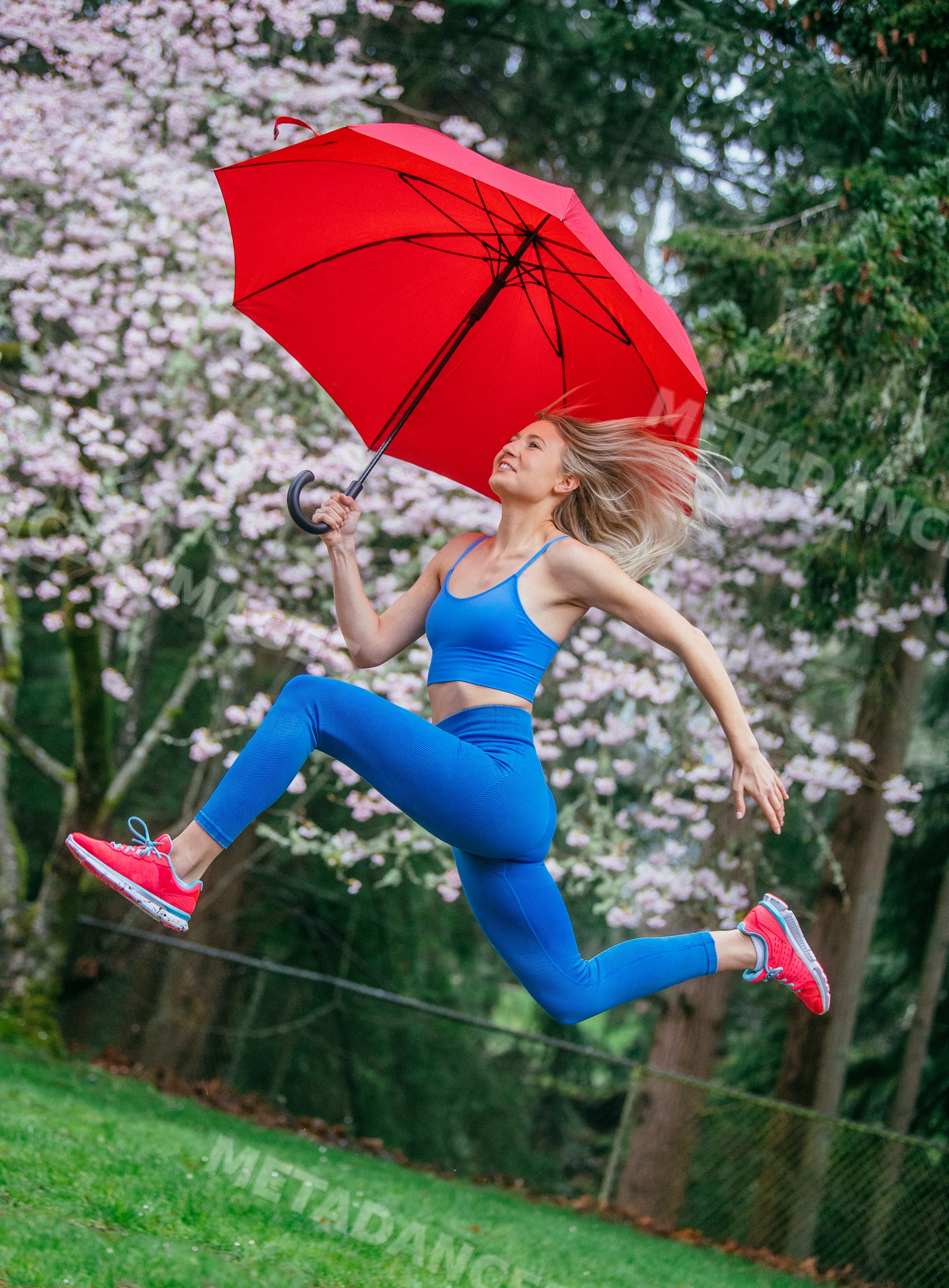 White woman jumping with red umbrella in park with cherry blossoms