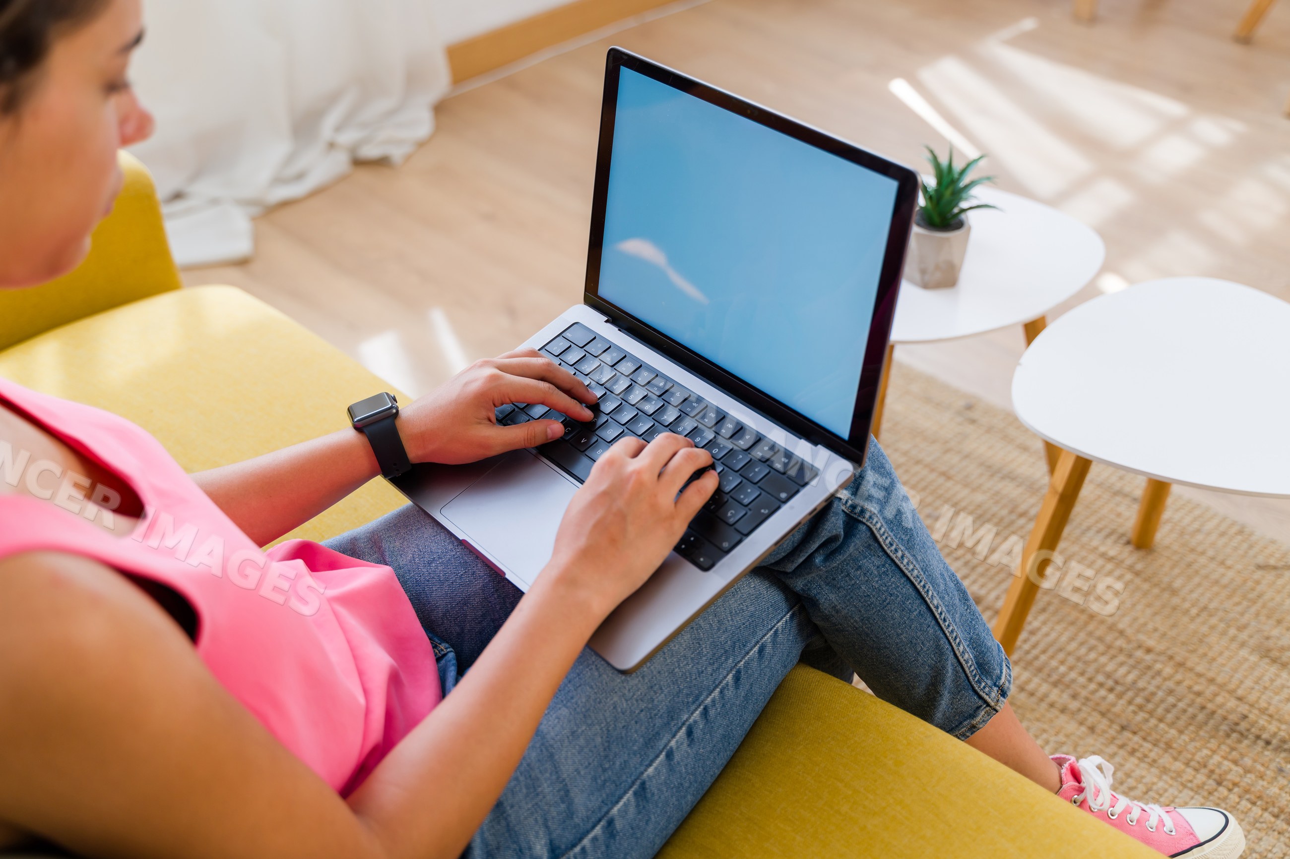 A Hispanic woman types on a laptop in a modern living room